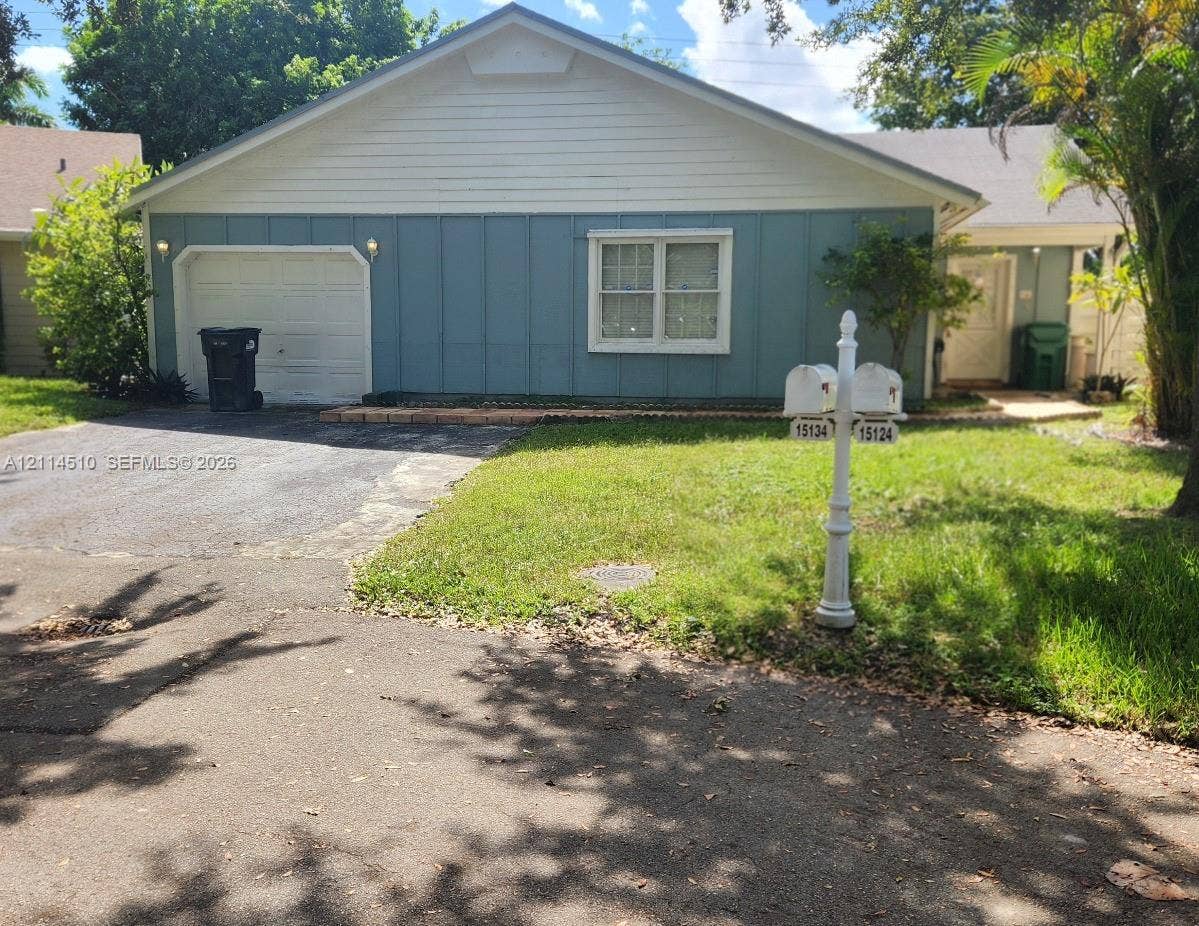 15134 SW 142nd Place, Miami, FL 33186 Single-story exterior featuring blue vertical siding, a gabled roof, an attached one-car garage, and a concrete driveway