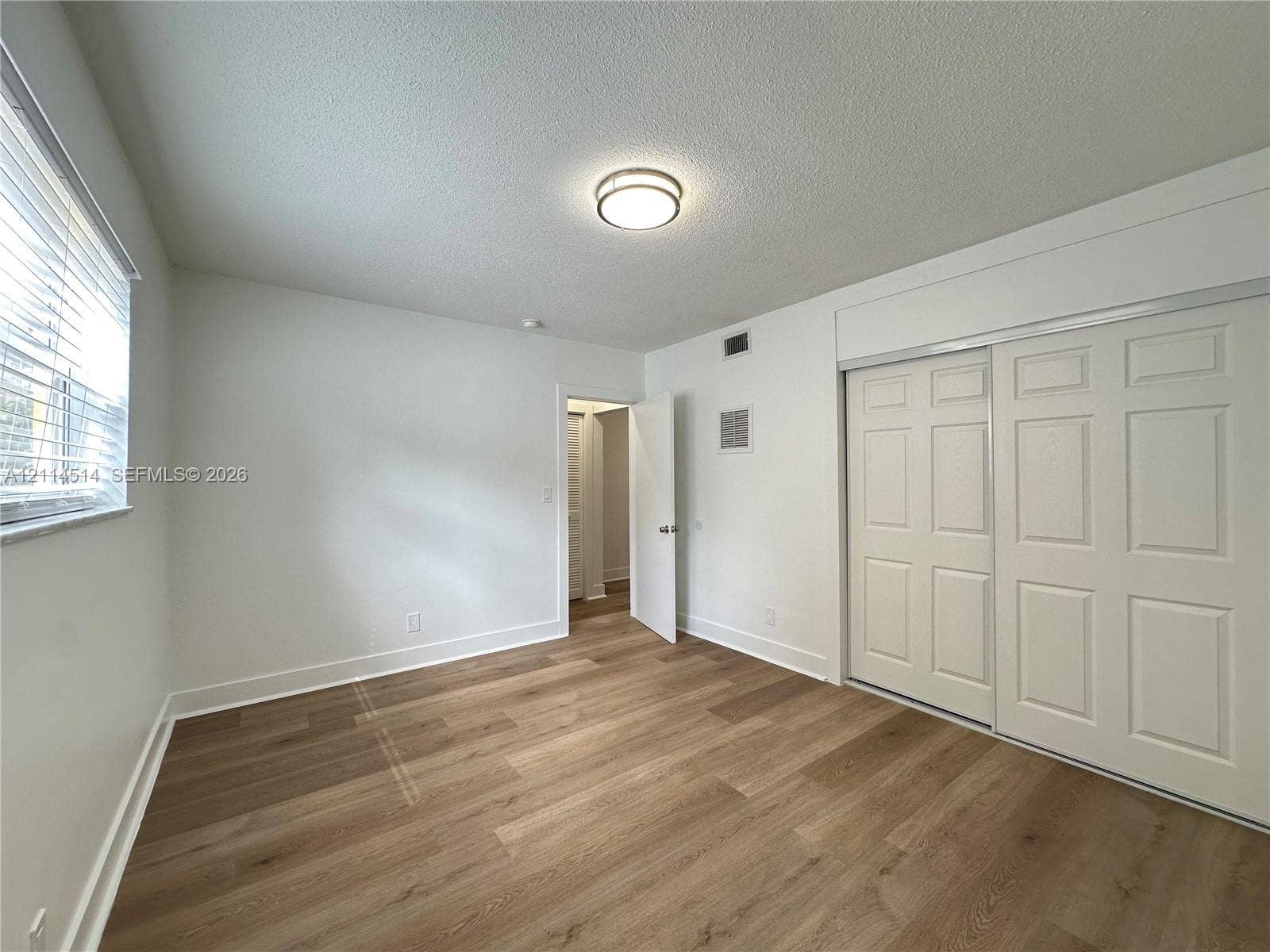 Room featuring wood-finish flooring, sliding closet doors with paneled detailing, neutral wall finishes, and a flush-mount circular lighting fixture