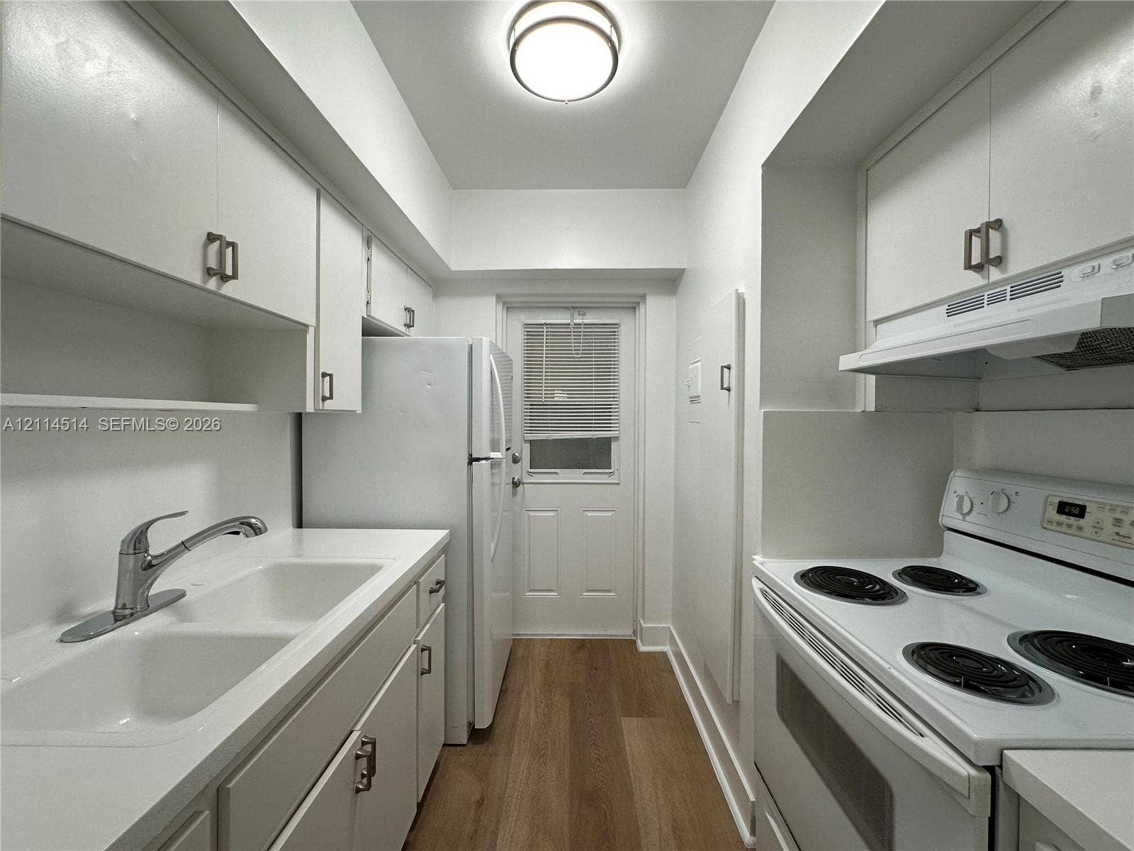 Galley kitchen featuring white cabinetry, dual-basin sink with chrome faucet, integrated range hood, white electric range, and wood-finish flooring
