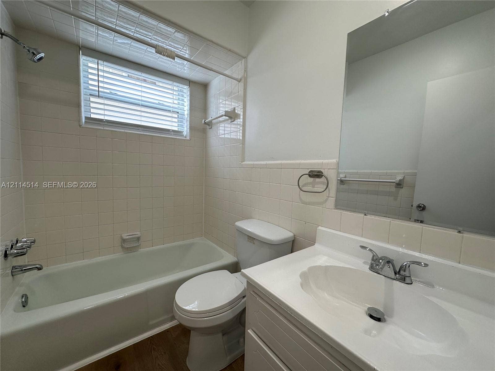 Bathroom featuring a vanity with a white integrated sink, chrome dual-handle faucet, wall-mounted mirror, and tile-surround shower and bathtub combination