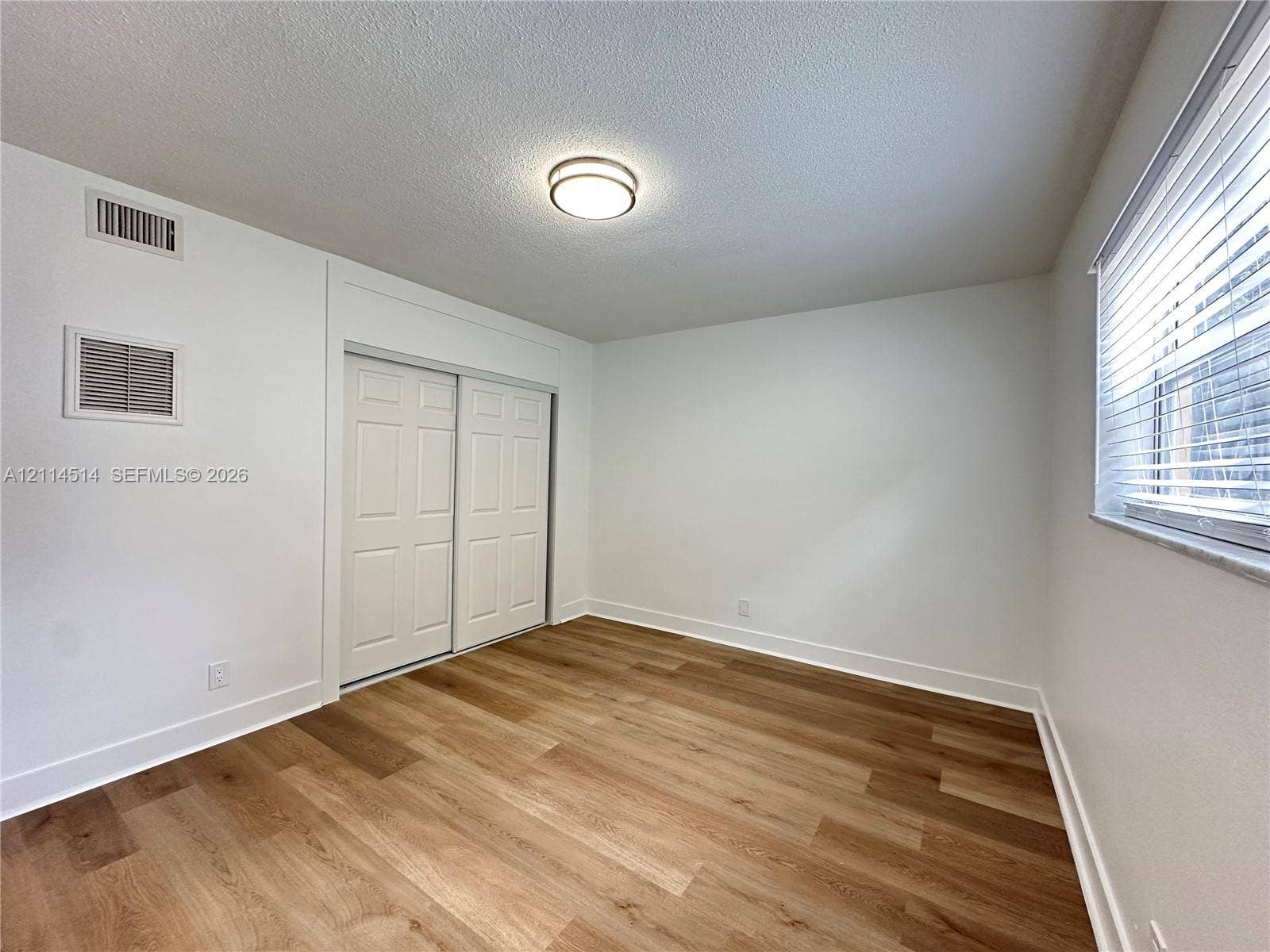 Neutral interior space featuring wood-finish flooring, sliding closet doors with raised panel detail, and a flush-mount circular ceiling fixture