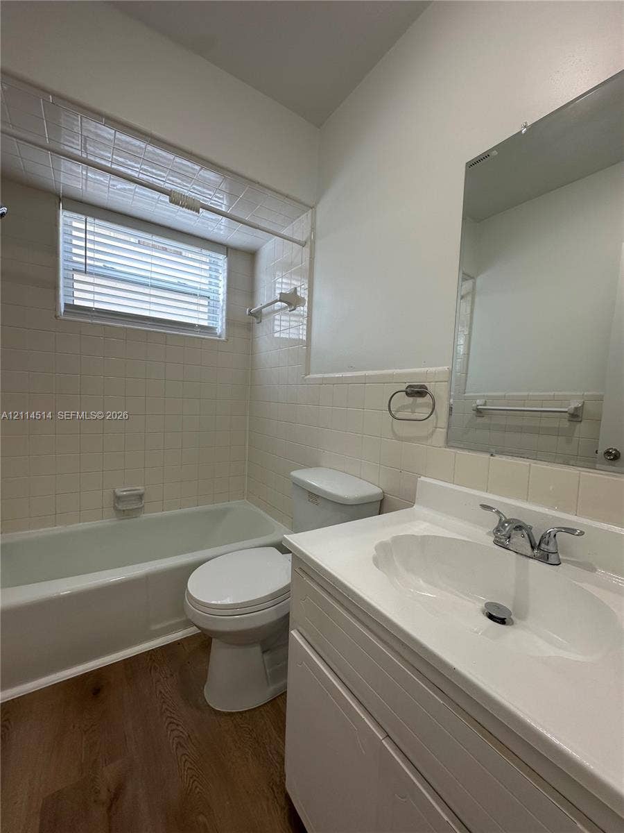 Bathroom featuring a white vanity with an integrated basin, wood-finish flooring, tiled shower surround, and a recessed mirror