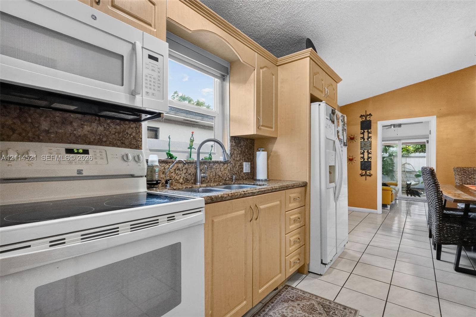 Kitchen featuring light-finish wood cabinetry, integrated white appliances, stone-texture countertops, double-basin stainless steel sink, and ceramic tile flooring