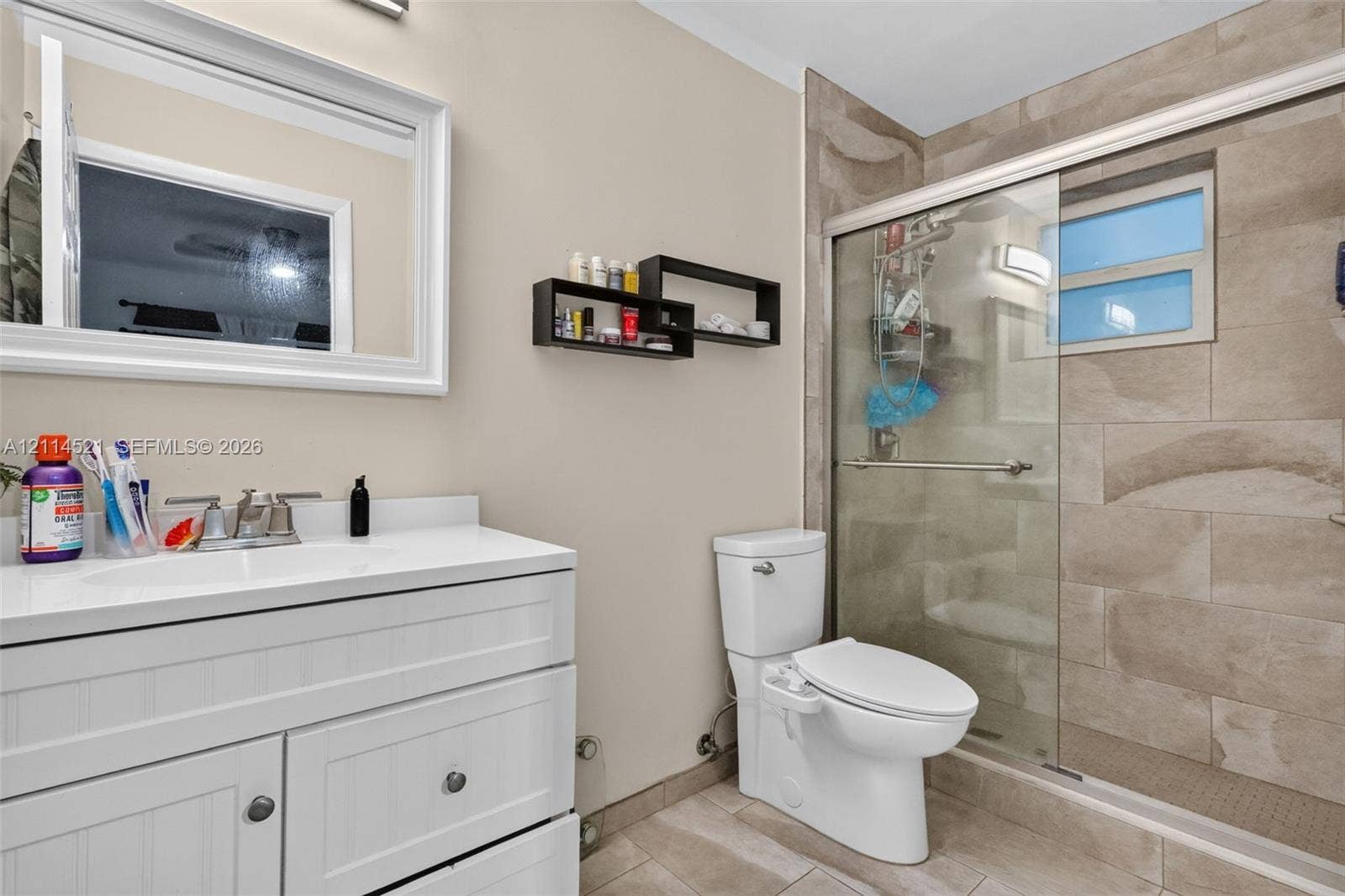 Bathroom featuring a white shaker-style vanity with an integrated countertop, a framed rectangular mirror, and a walk-in shower with stone-finish tile surround, sliding glass door, and recessed lighting