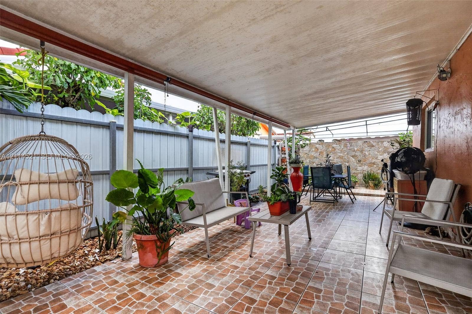 Covered patio featuring patterned tile flooring, a corrugated ceiling, and stone-textured privacy fencing