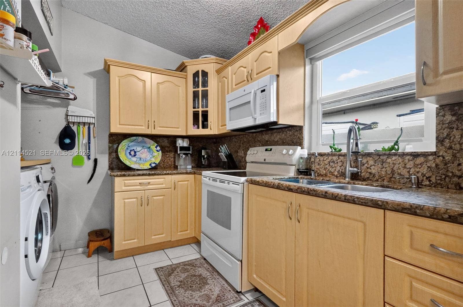 Kitchen featuring natural-finish wood cabinetry, stone-patterned countertops, a double-basin stainless steel sink with a goose-neck faucet, and white tile flooring