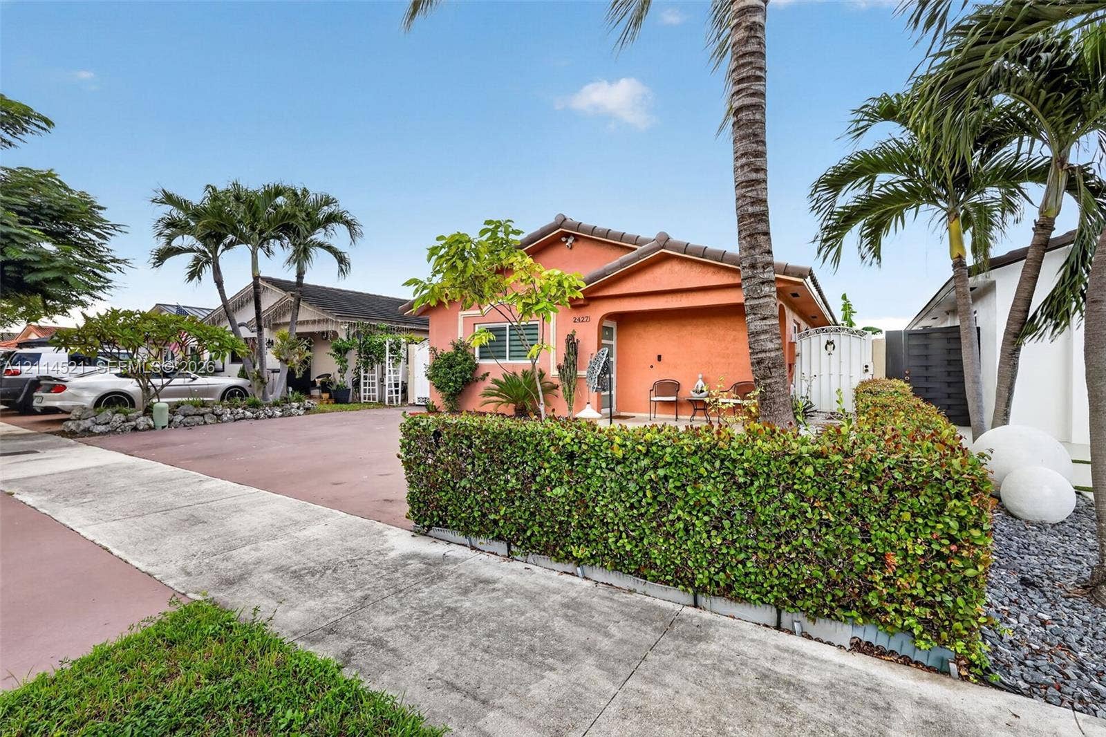 Stucco exterior residence featuring a covered front porch, paved driveway, and manicured hedge landscaping