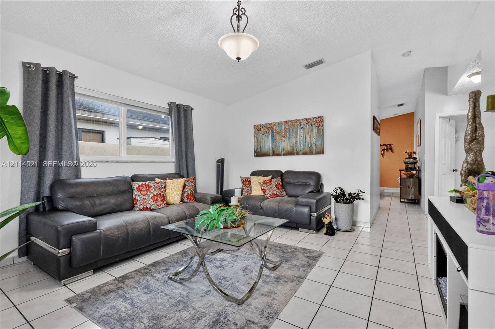 Living area featuring light-colored floor tiling, a single-hung window, and a central pendant light fixture