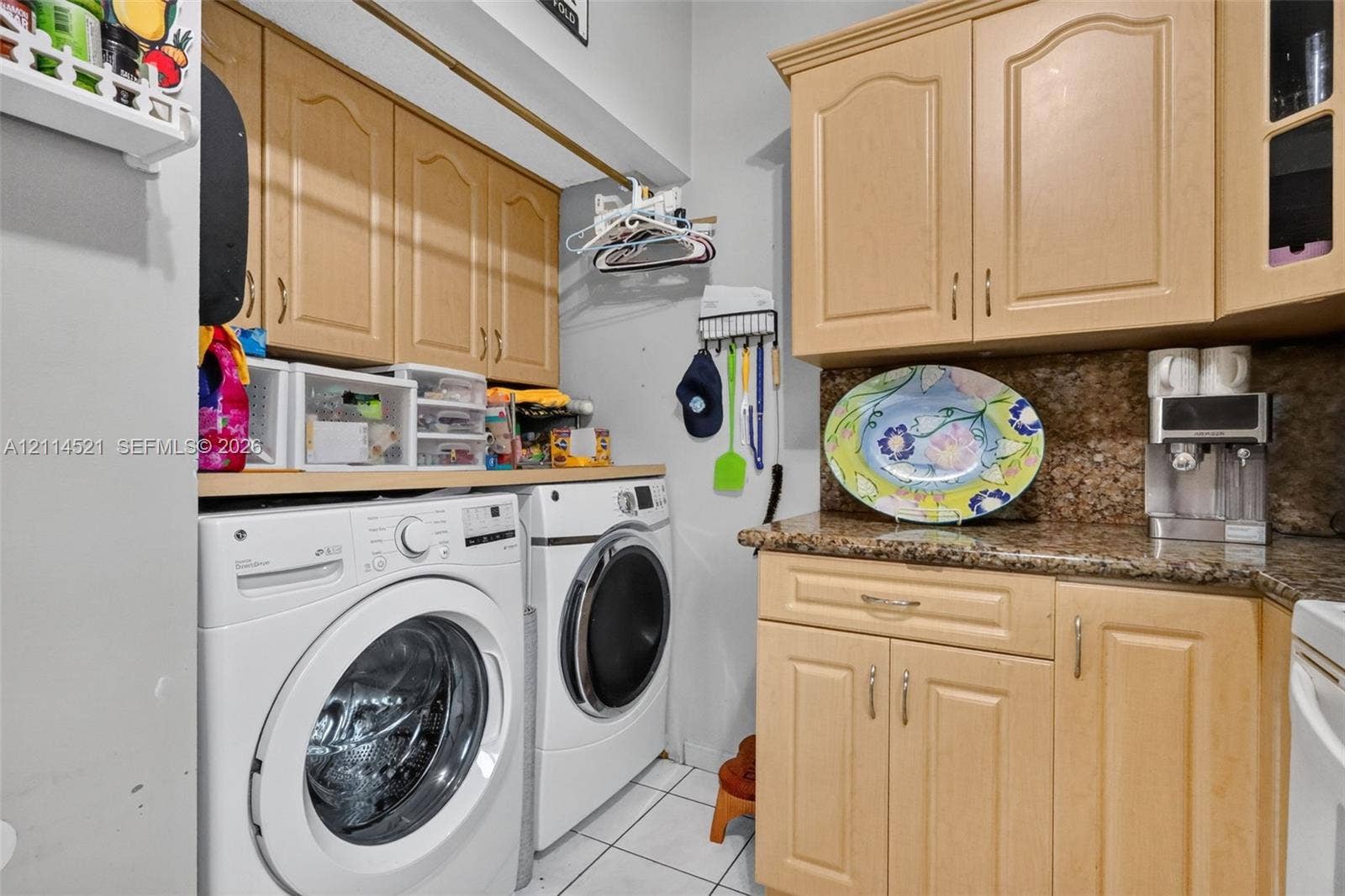 Utility space featuring raised-panel wood cabinetry, natural stone countertops, and tile flooring