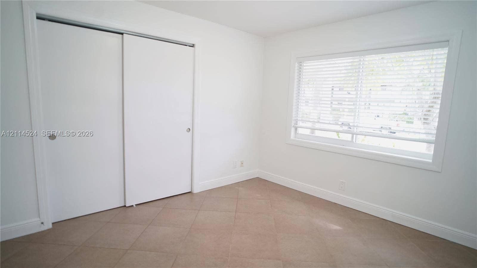 Neutral-toned tile flooring, white sliding closet doors, and a window with horizontal blinds