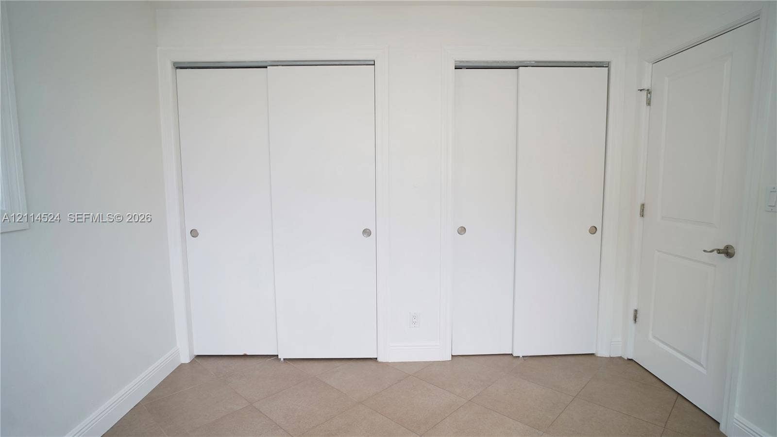 Dual floor-to-ceiling closets with sliding doors, neutral ceramic tile flooring, and a solid-core interior swing door