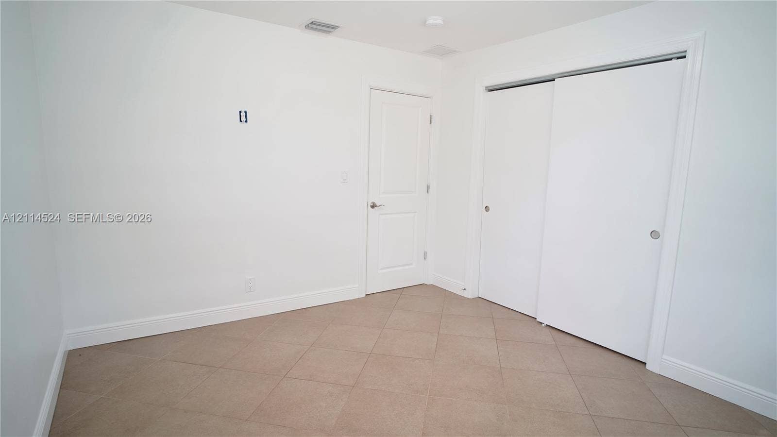 Neutral-toned tile flooring, solid-core interior door, and dual sliding-door closet with clean white finishes