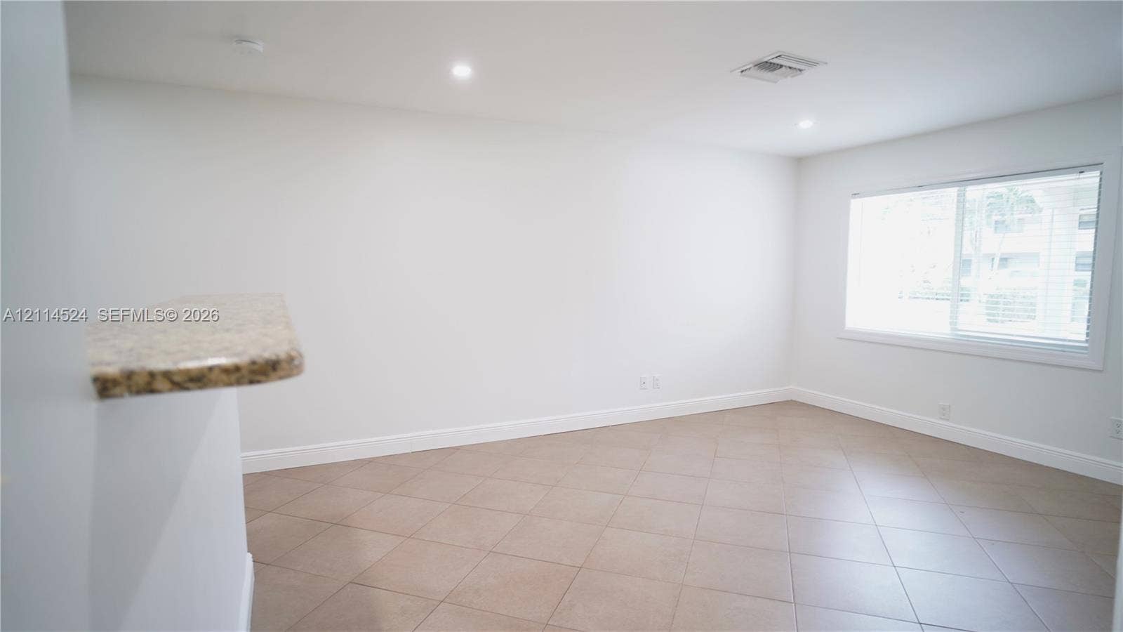 Interior space featuring large-format diagonal tile flooring, neutral walls, recessed lighting, and a breakfast bar with a stone-finish countertop
