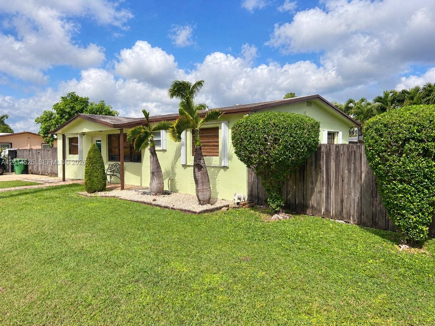 18905 SW 313th Terrace, Homestead, FL 33030 Single-story residence featuring light-toned exterior finish, low-slope roof, covered front entrance, wood-panel fencing, and mature landscaping