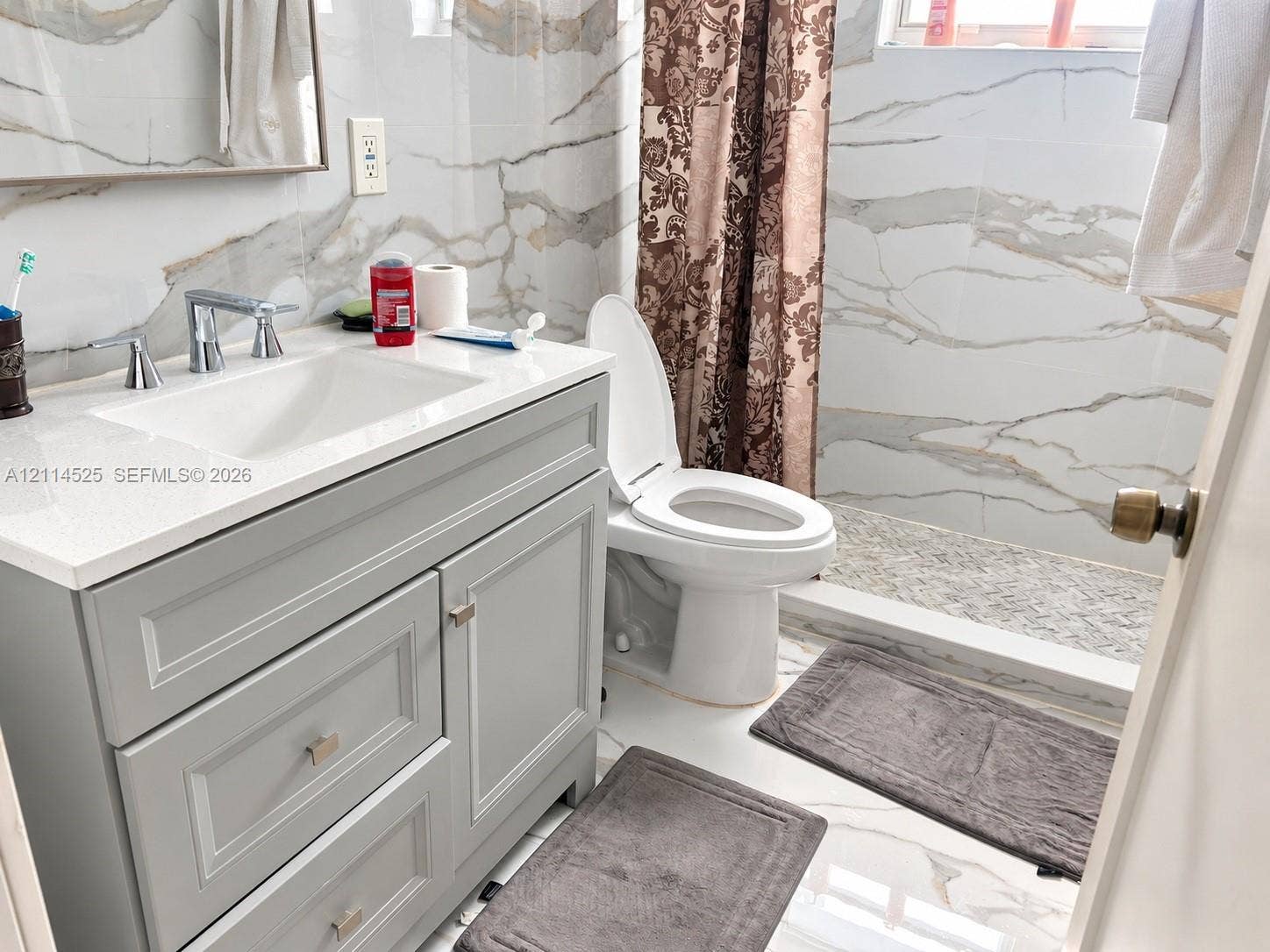 18905 SW 313th Terrace, Homestead, FL 33030 Bathroom featuring a grey shaker-style vanity with a solid surface countertop, an undermount sink with a polished chrome faucet, and large-format wall tiling with a vein pattern