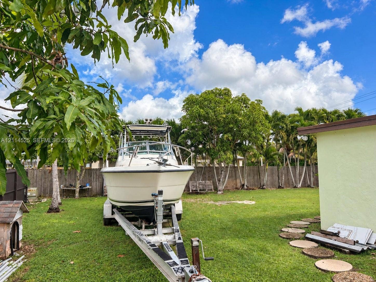 18905 SW 313th Terrace, Homestead, FL 33030 Expansive backyard featuring a level lawn, perimeter wood fencing, and mature trees with stone paver accents
