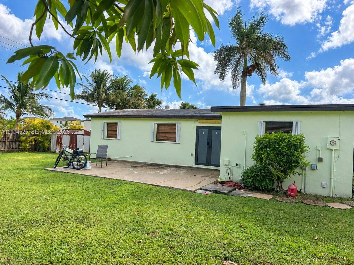 18905 SW 313th Terrace, Homestead, FL 33030 Rear exterior featuring a concrete patio, double entry doors, and an expansive lawn with mature palm trees