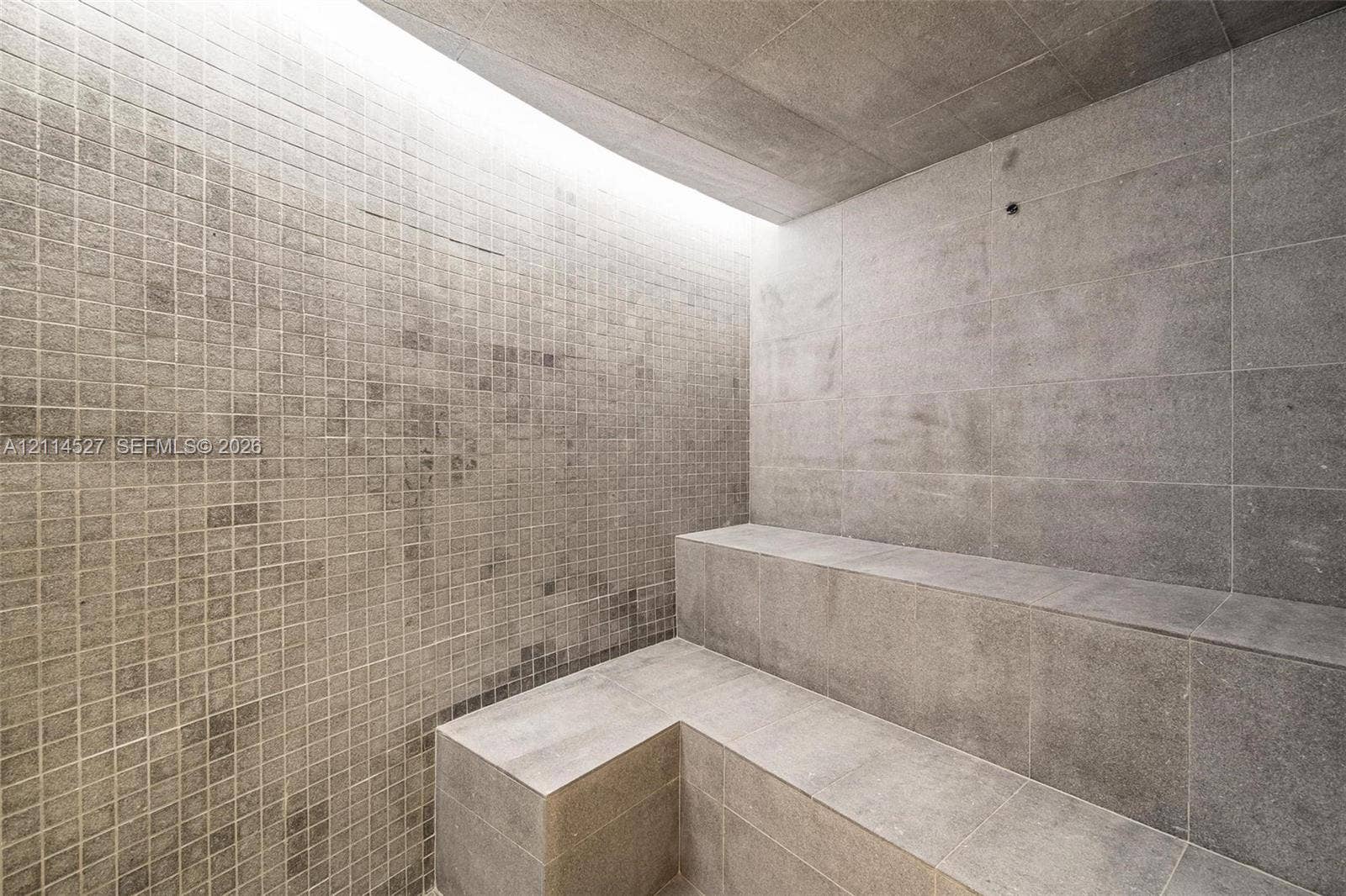 Steam room featuring tiered stone bench seating, full-height wall tiling in a mosaic pattern, large-format stone floor and wall tiles, and integrated recessed lighting