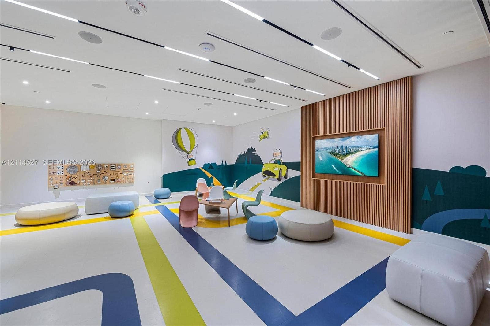 Open-concept room featuring a linear recessed lighting system, integrated ceiling speakers, and a wood-slat accent wall with a wall-mounted display