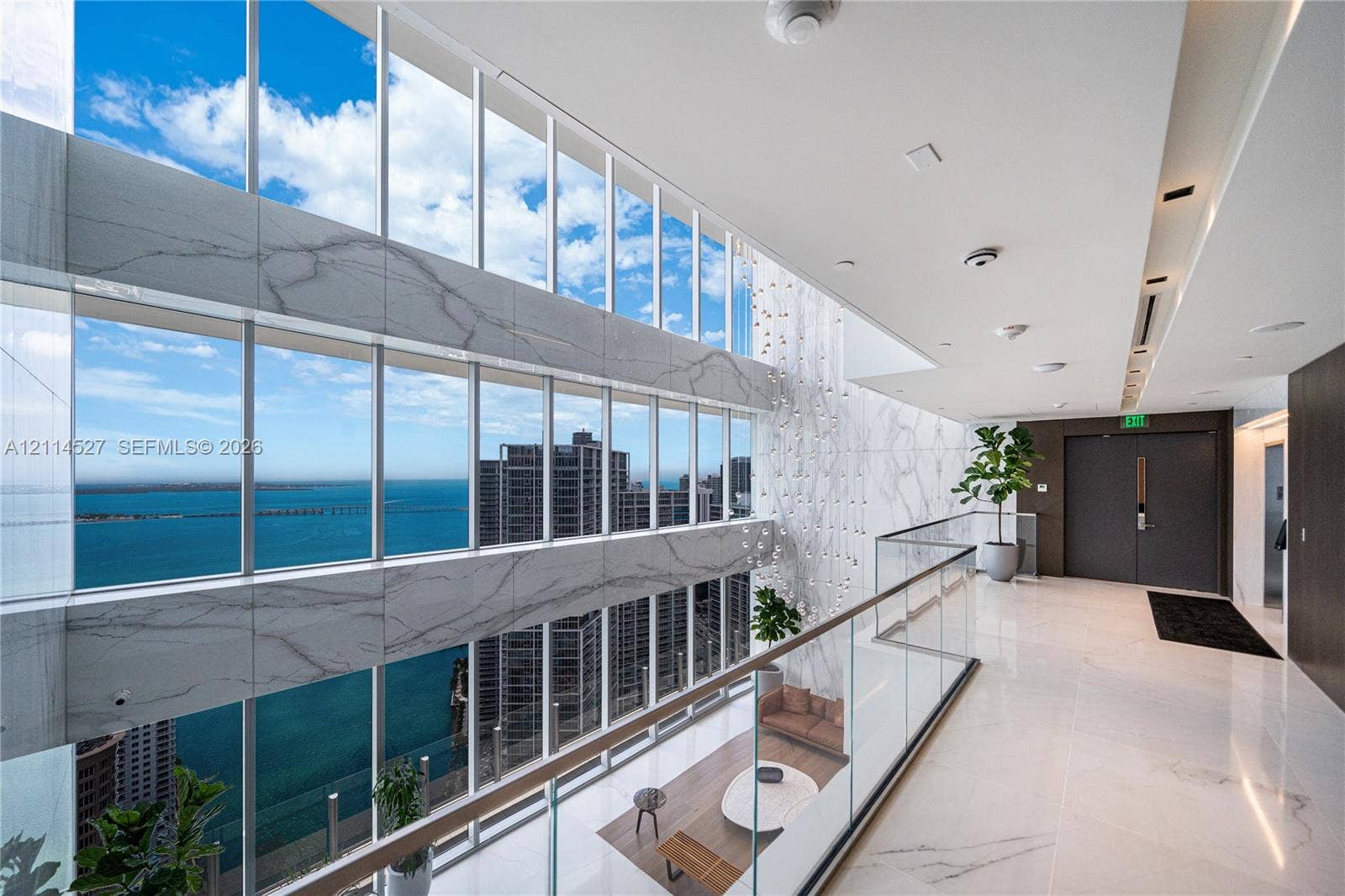 Double-height floor-to-ceiling windows featuring large-format stone wall cladding, glass balcony railing, polished stone flooring, and recessed ceiling lighting