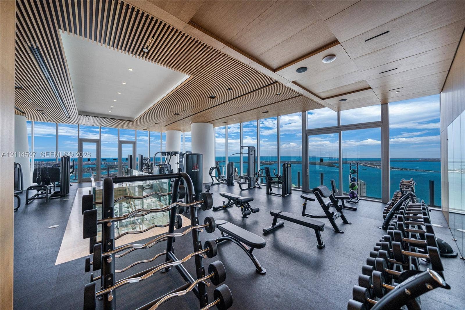 Fitness space featuring floor-to-ceiling windows, wood-paneled slat ceiling, rubberized flooring, and structural columns