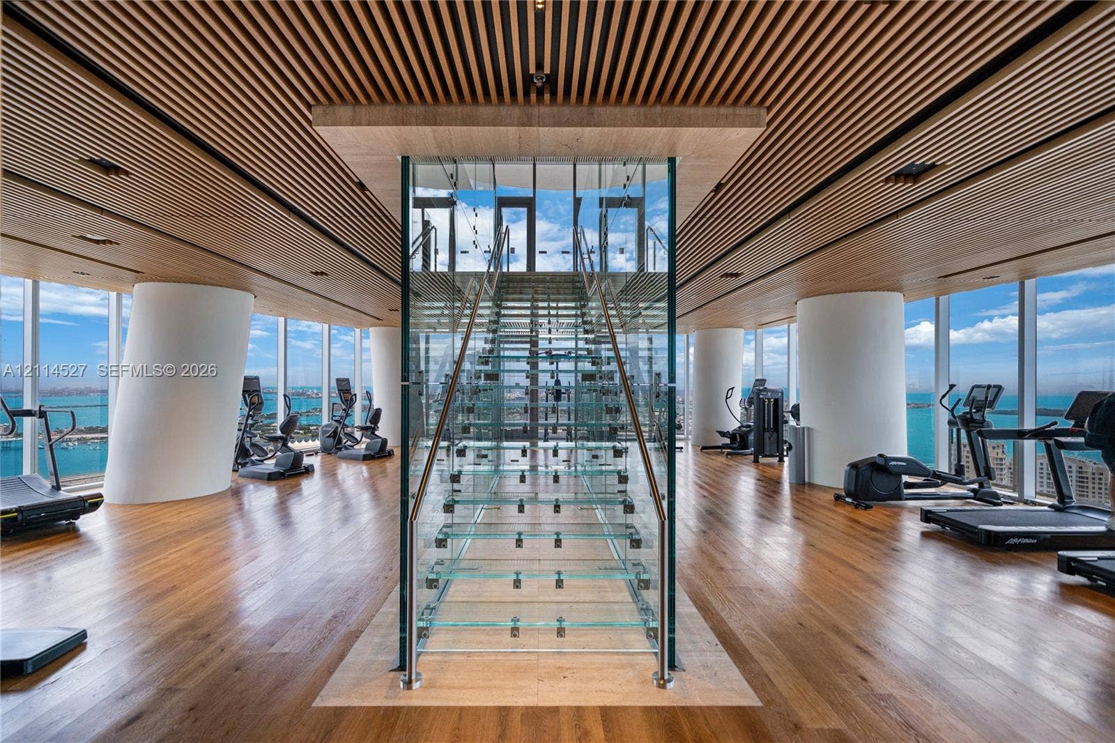 Wood-slat ceiling, floor-to-ceiling glass walls, central floating glass staircase with metal railings, and wood-finish flooring