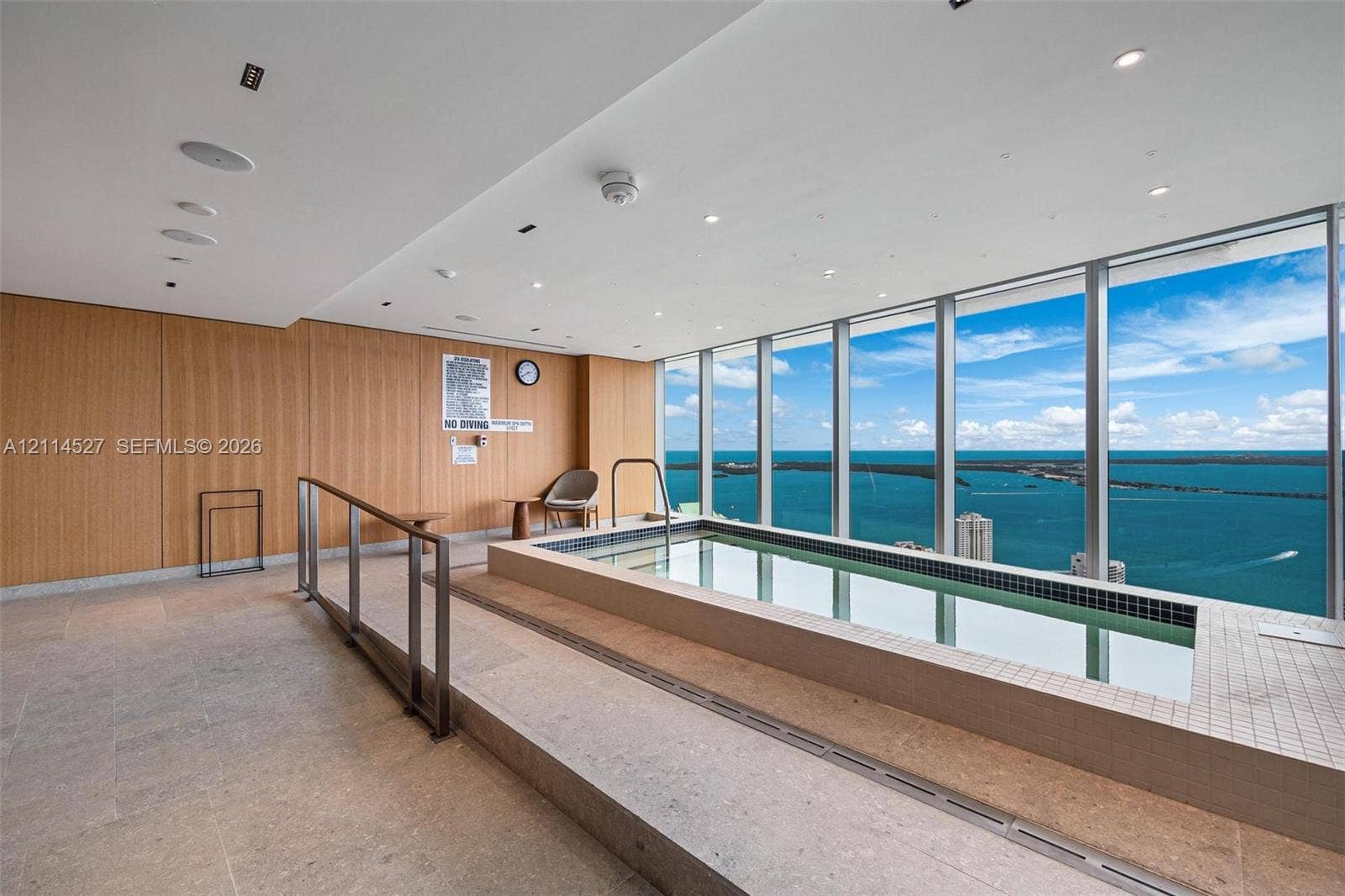 Indoor pool with tile surround, wood-finish paneling, floor-to-ceiling windows, and recessed lighting