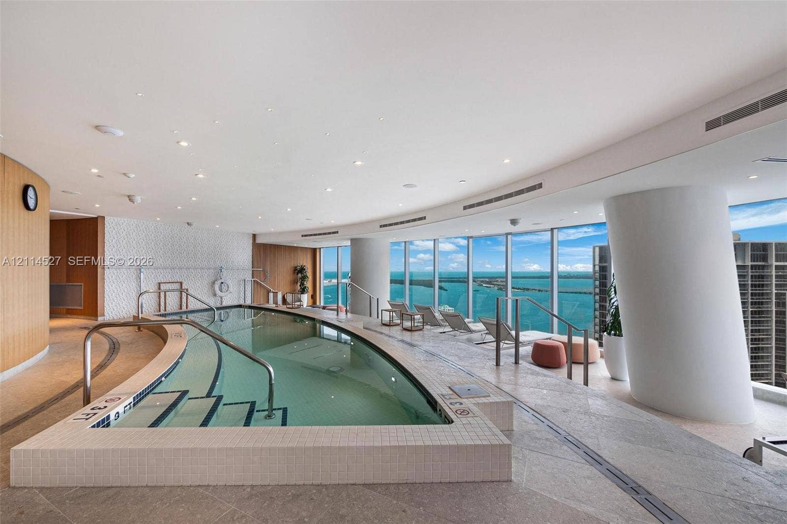 Indoor pool area featuring floor-to-ceiling windows, stone tile flooring, recessed ceiling lighting, and custom curved architectural columns