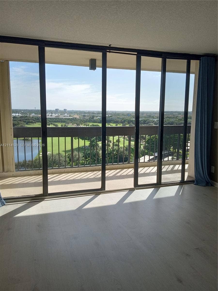 2400 Presidential Way, #1205, West Palm Beach, FL 33401 Floor-to-ceiling sliding glass doors opening to a private balcony with metal railing, wood-finish flooring, and expansive natural scenery