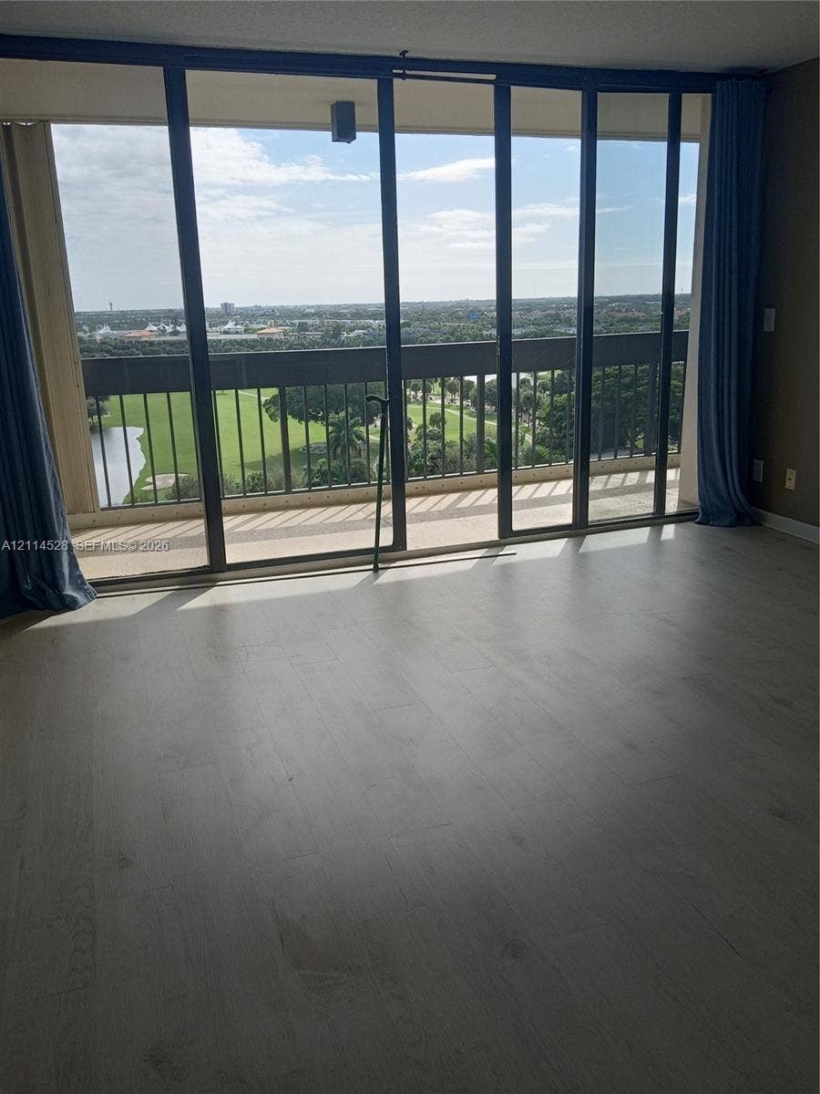 2400 Presidential Way, #1205, West Palm Beach, FL 33401 Floor-to-ceiling sliding glass panels, light-tone wood-finish flooring, and a private balcony with metal railings overlooking the landscape