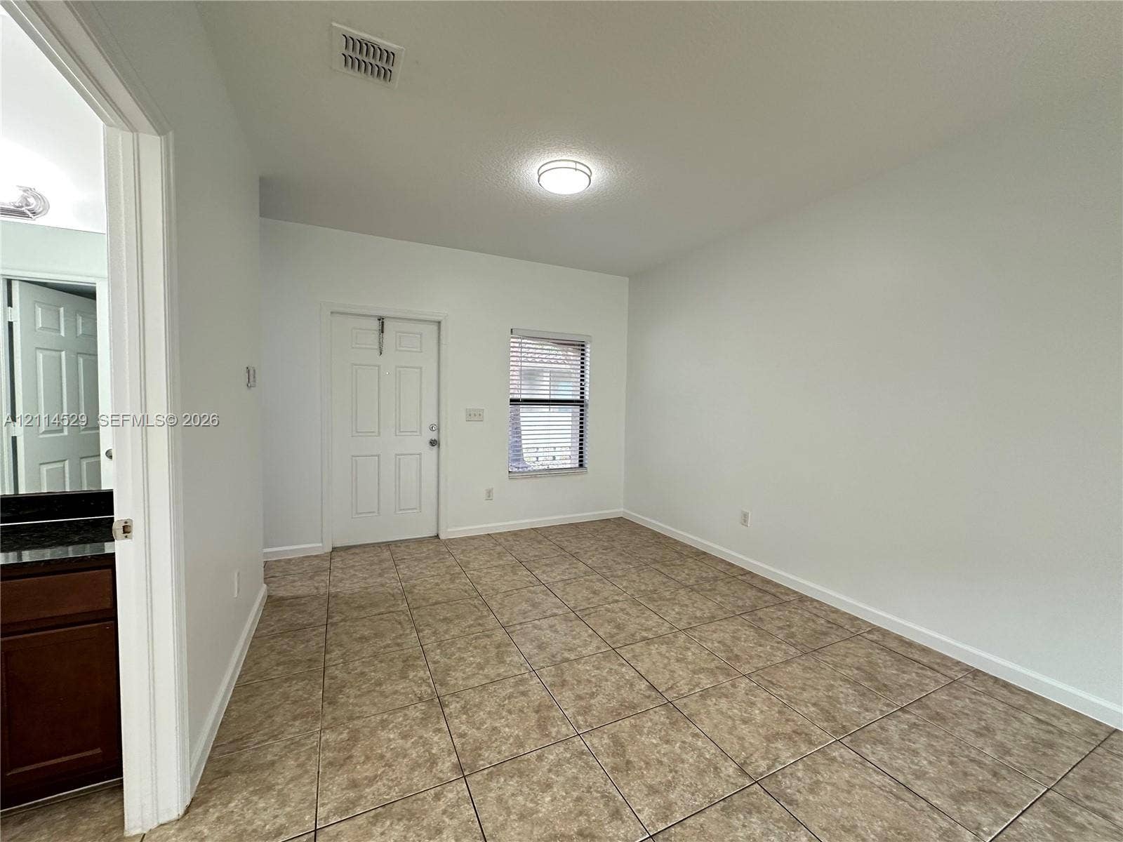 Interior space featuring neutral-toned tile flooring, a six-panel door, and a flush-mount ceiling light fixture