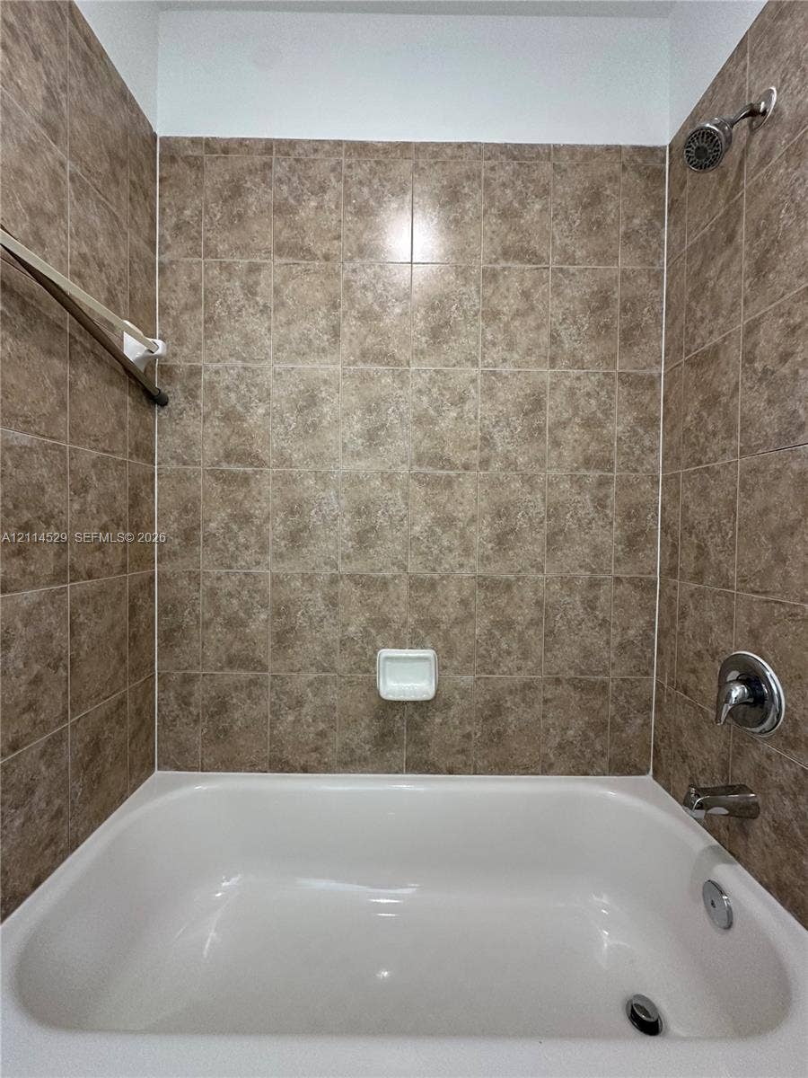 Bathtub surround featuring floor-to-ceiling square ceramic tiles, a built-in recessed soap dish, and polished chrome shower and tub fixtures