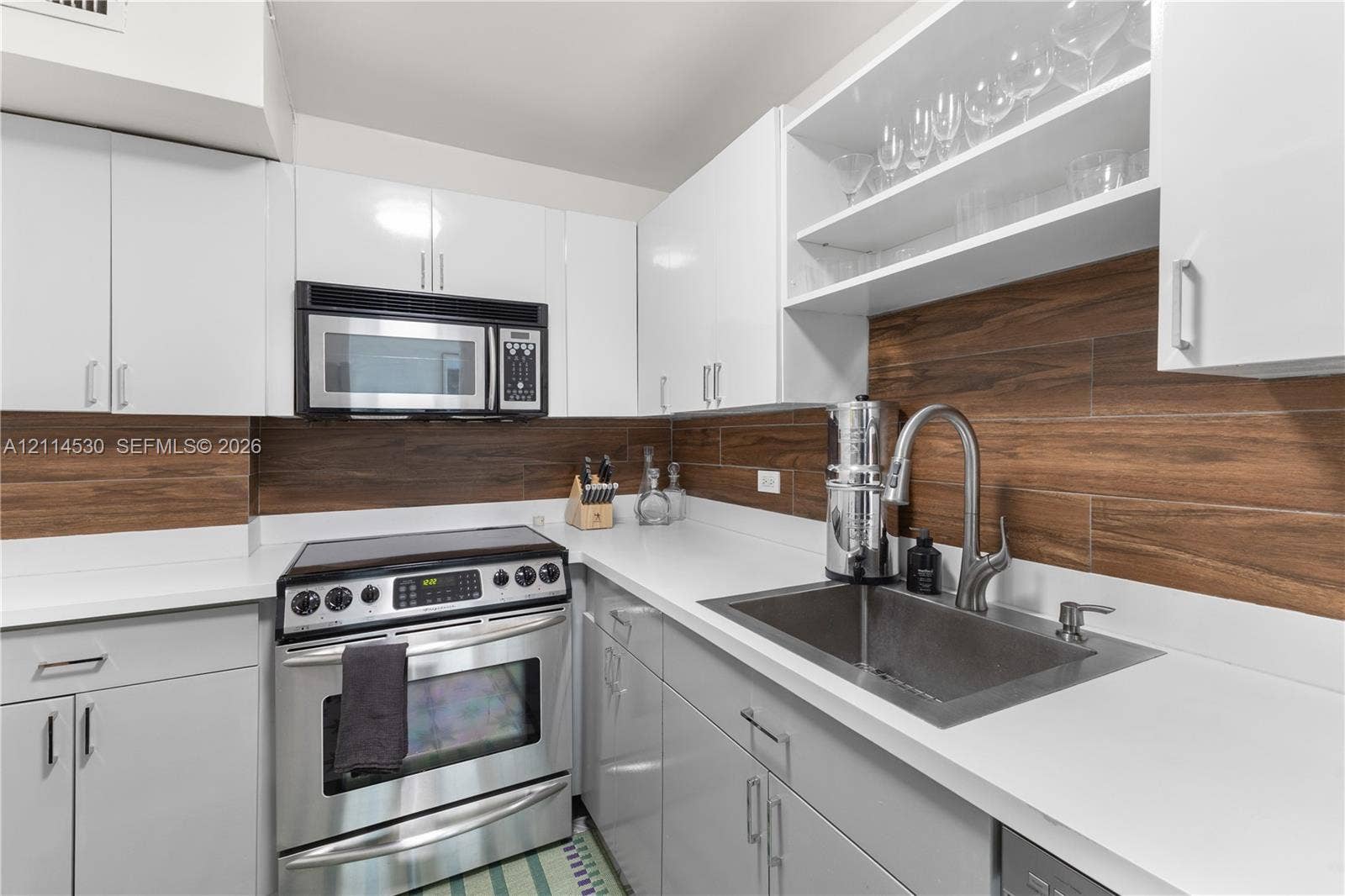 3 Island Avenue, #14L, Miami Beach, FL 33139 Kitchen featuring white flat-panel cabinetry, quartz countertops, stainless steel appliances, wood-finish tile backsplash, and open shelving