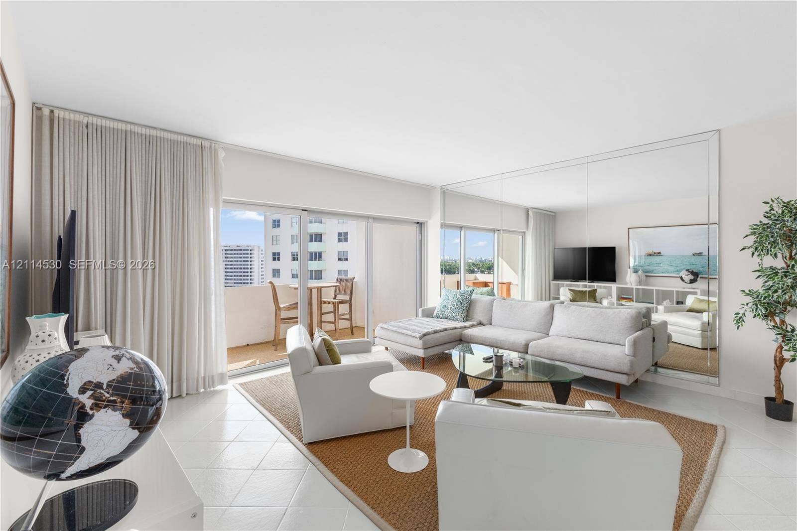 3 Island Avenue, #14L, Miami Beach, FL 33139 Light-filled living area featuring floor-to-ceiling glass sliding doors, neutral tile flooring, and a full-height mirrored wall