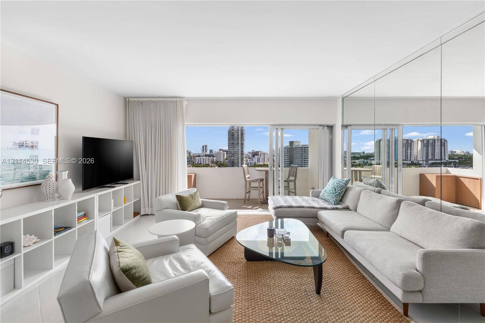 3 Island Avenue, #14L, Miami Beach, FL 33139 Living area featuring floor-to-ceiling mirrored walls, custom built-in white shelving, sliding glass balcony doors, and panoramic city skyline scenery