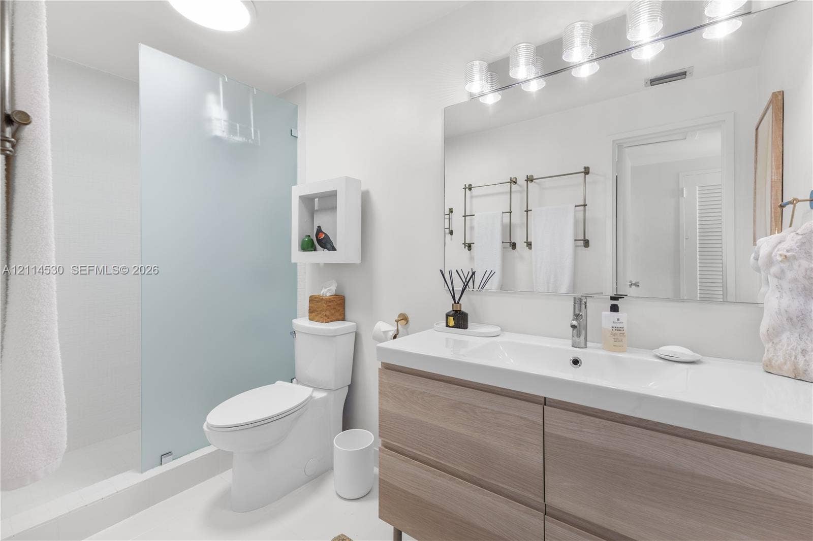 3 Island Avenue, #14L, Miami Beach, FL 33139 Bathroom featuring a floating vanity with a seamless integrated sink, wood-finish cabinetry, a large wall-mounted mirror, a walk-in shower with a frosted glass panel, and built-in recessed wall shelving