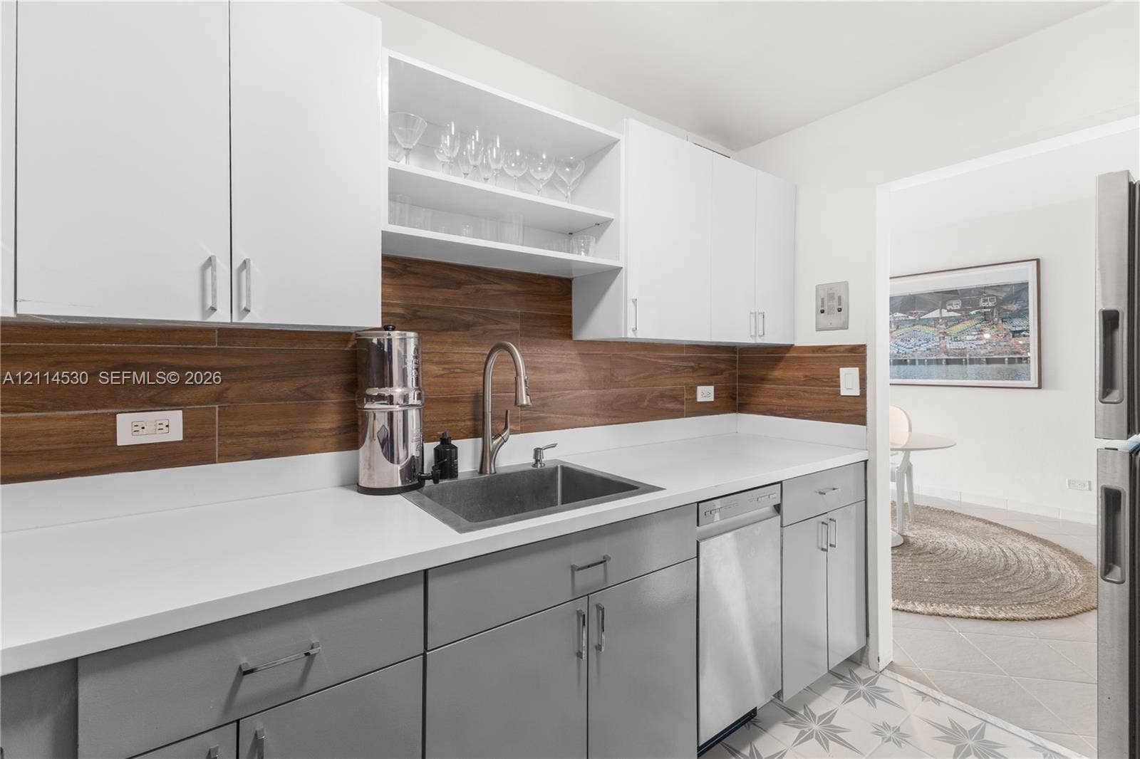 3 Island Avenue, #14L, Miami Beach, FL 33139 Kitchen featuring white upper cabinetry, grey lower cabinetry, wood-tone backsplash, solid-surface countertops, and an undermount sink with a high-arch faucet