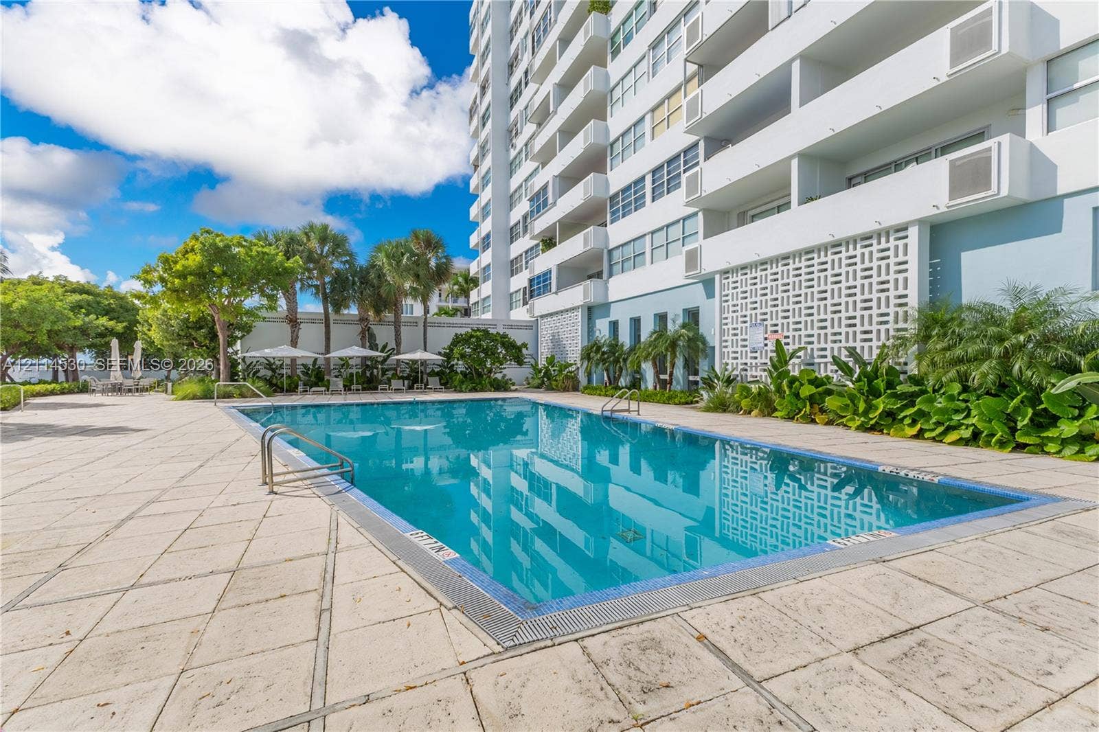 3 Island Avenue, #14L, Miami Beach, FL 33139 In-ground swimming pool with tile border, expansive stone-paver deck, decorative concrete privacy screen, and mature perimeter landscaping