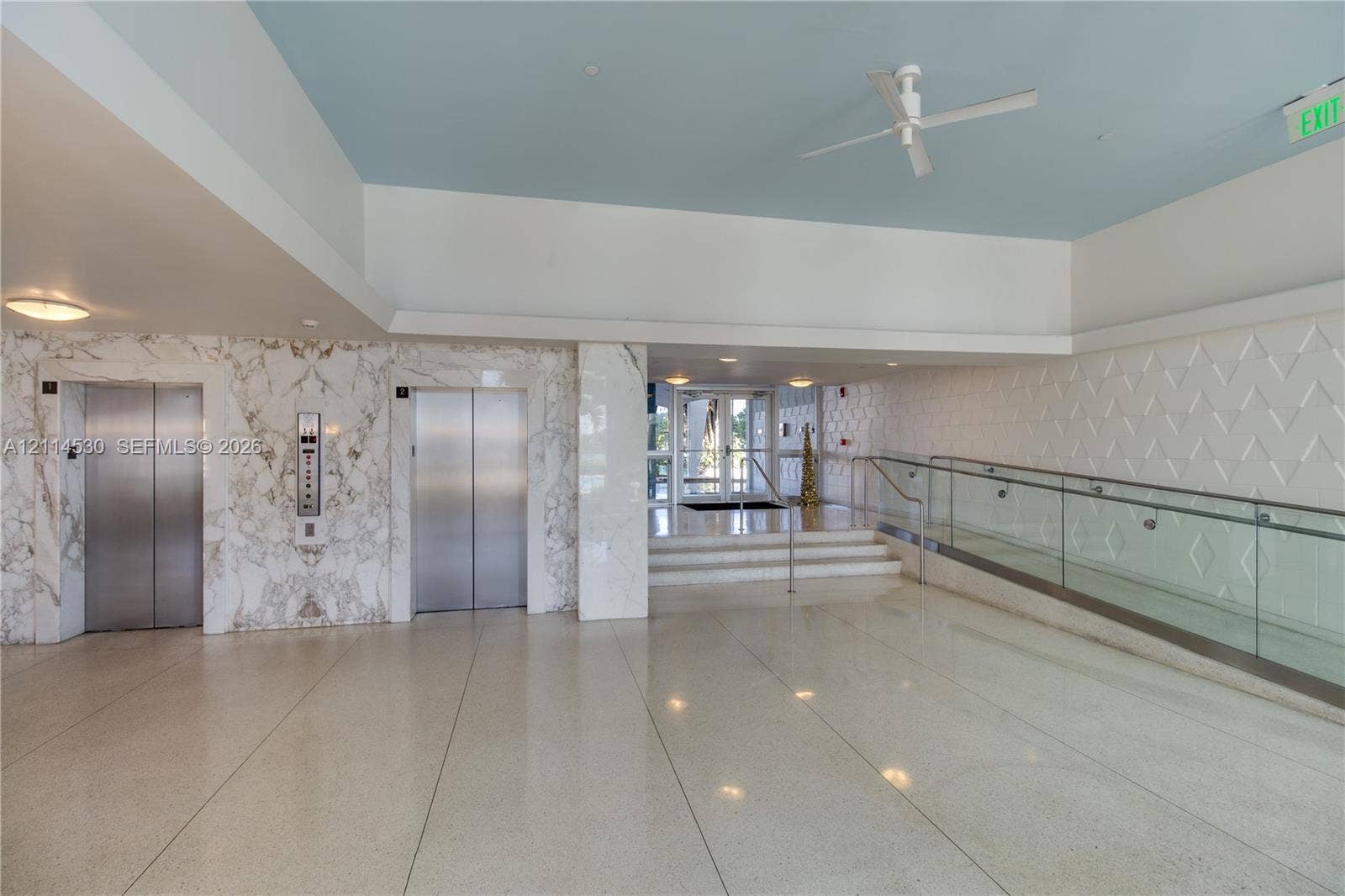 3 Island Avenue, #14L, Miami Beach, FL 33139 Lobby area featuring dual stainless-steel elevators, stone-paneled accent walls, polished stone flooring, a glass-panel ramp railing, and textured wall detailing