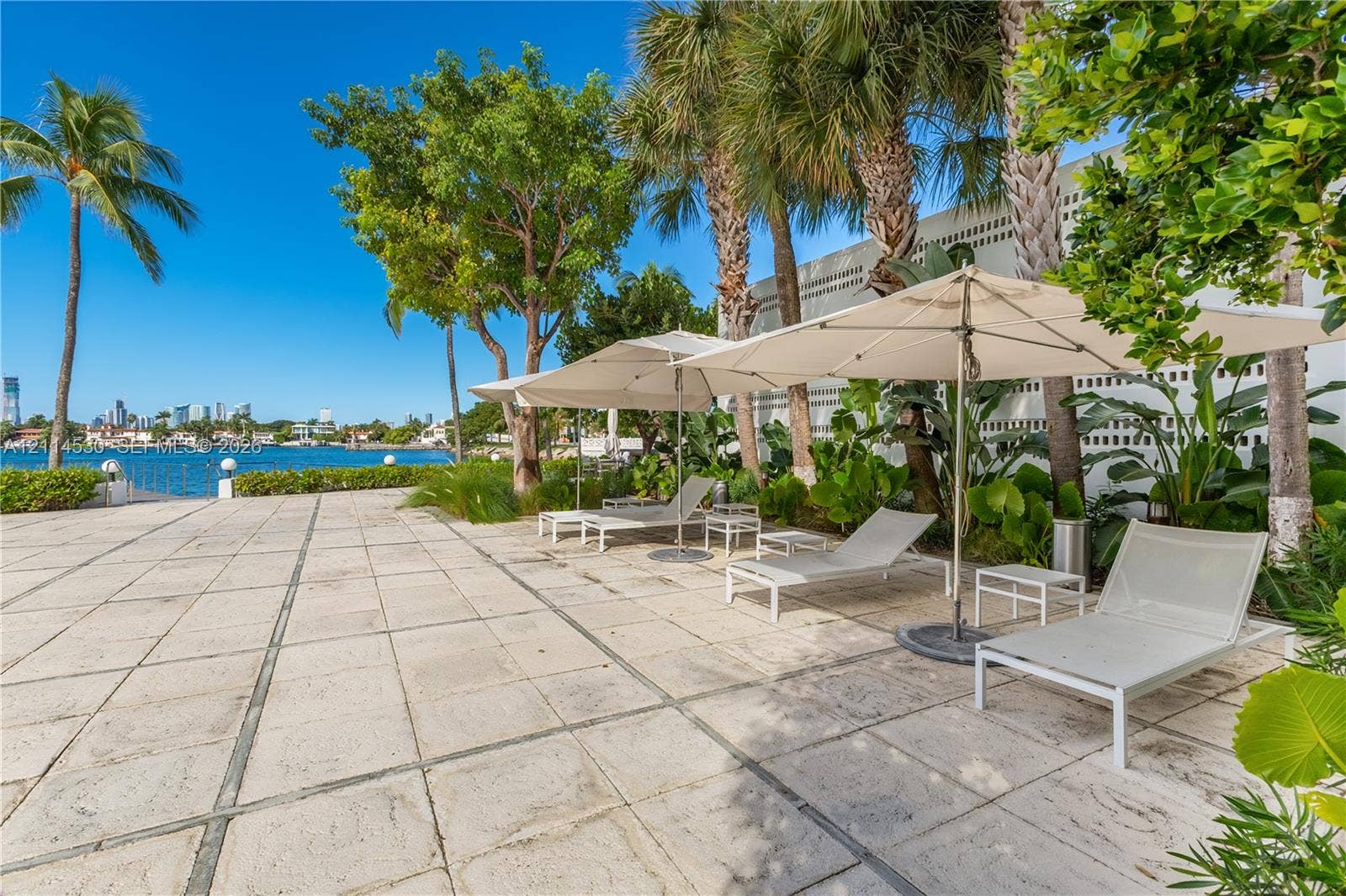 3 Island Avenue, #14L, Miami Beach, FL 33139 Waterfront patio featuring expansive stone tile pavers, mature palm trees, lush tropical landscaping, and a decorative concrete masonry wall