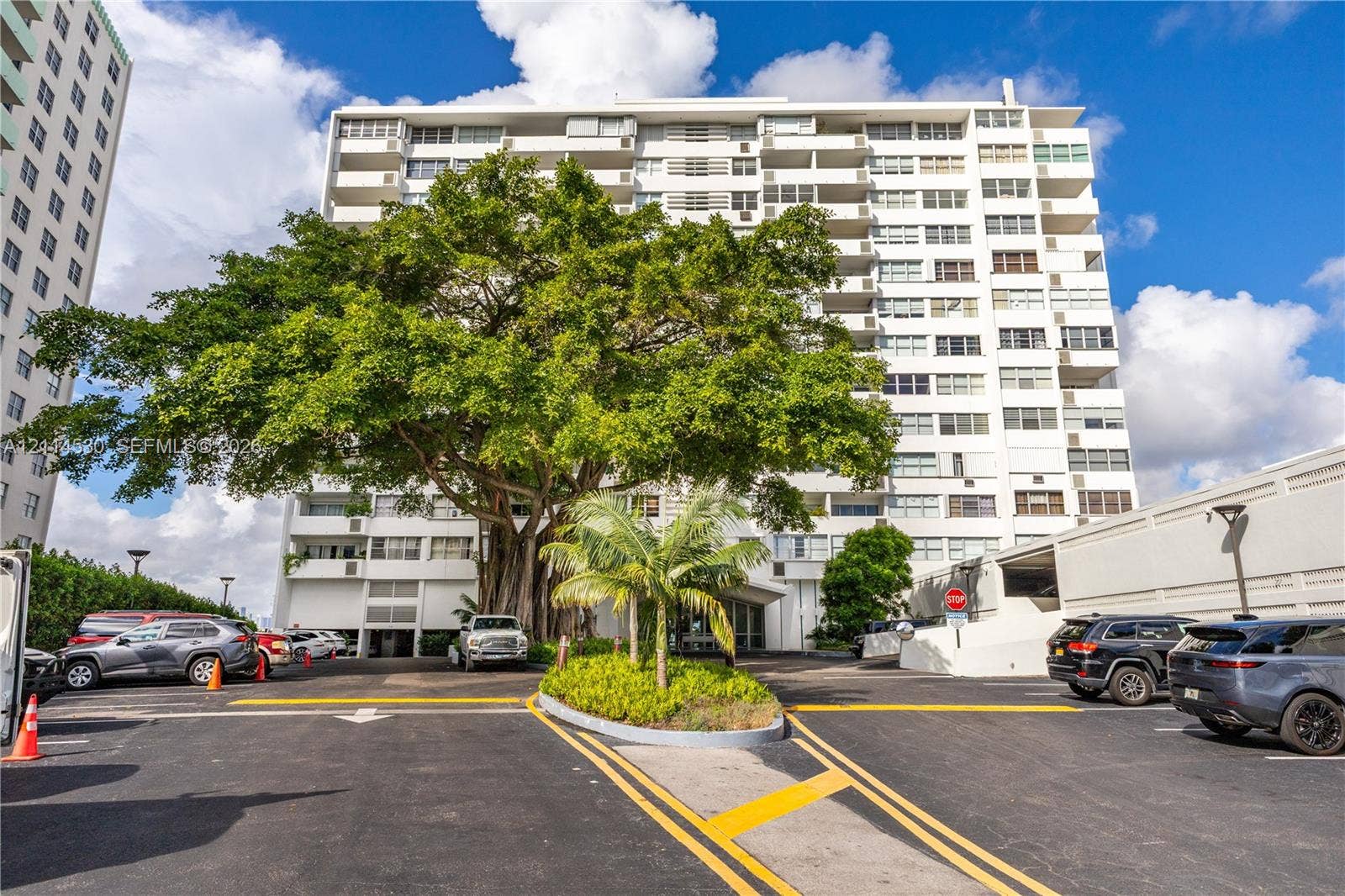 3 Island Avenue, #14L, Miami Beach, FL 33139 Mid-rise residential building featuring private balcony levels, ground-level surface parking, mature specimen trees, and established landscaping