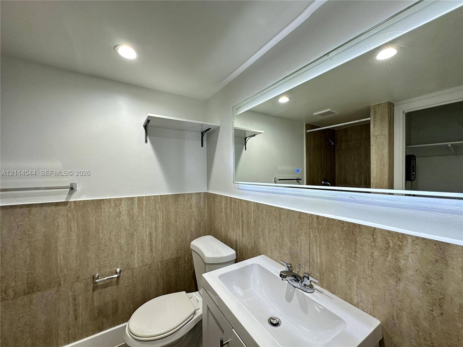 1413 N Dixie Highway, #3, Fort Lauderdale, Fort Lauderdale, FL 33304 Bathroom featuring floor-to-ceiling stone-tile wainscoting, a vanity with an integrated basin, a polished chrome faucet, and a large wall-mounted mirror with integrated illumination