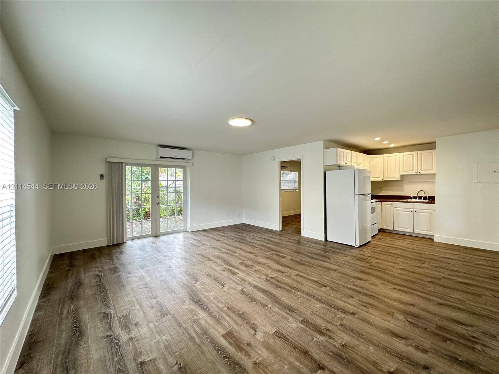 1413 N Dixie Highway, #3, Fort Lauderdale, Fort Lauderdale, FL 33304 Open-concept interior featuring wood-finish flooring, glass-paned double doors, wall-mounted climate control unit, and white cabinetry with integrated kitchen appliances