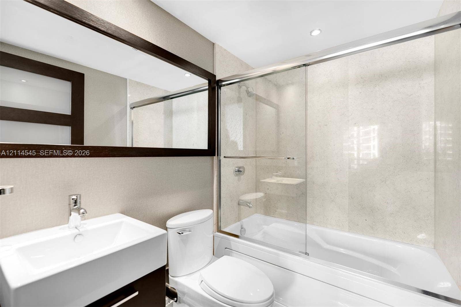 5875 Collins Avenue, #1503, Miami Beach, FL 33140 Bathroom featuring a vanity with an integrated rectangular sink, large framed mirror, soaking tub with glass sliding enclosure, and light-toned tile surround