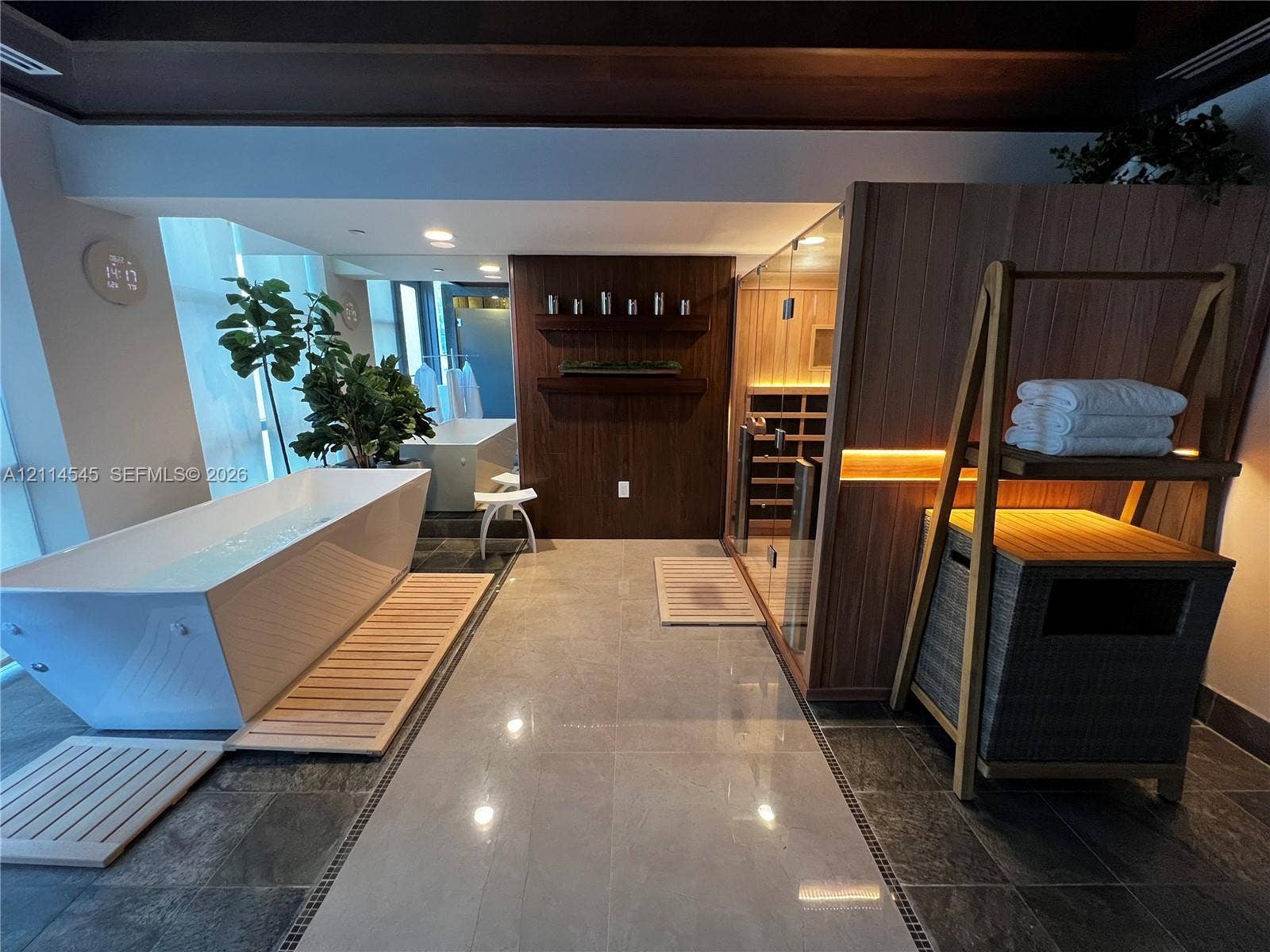 5875 Collins Avenue, #1503, Miami Beach, FL 33140 Freestanding soaking tub, glass-enclosed wood sauna with interior lighting, wood-paneled accent wall with built-in shelving, large-format tile flooring, and dark wood ceiling beams