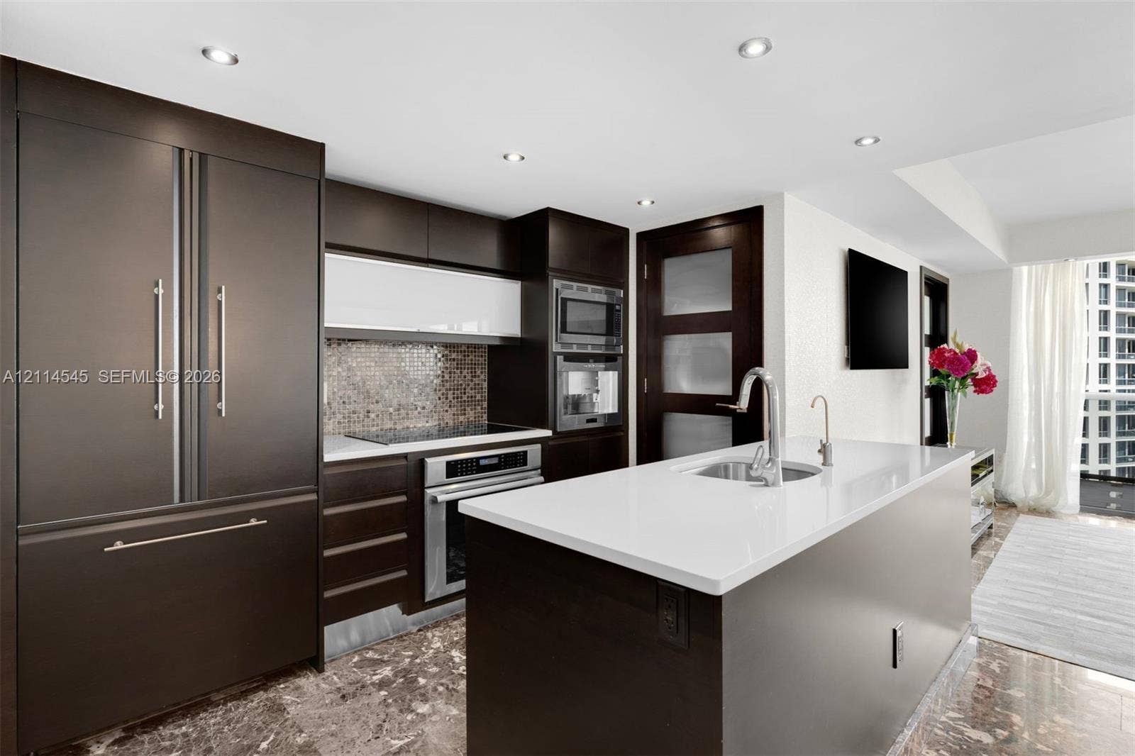 5875 Collins Avenue, #1503, Miami Beach, FL 33140 Modern kitchen featuring dark cabinetry, quartz-topped center island with integrated sink, stainless steel built-in appliances, recessed lighting, and stone flooring
