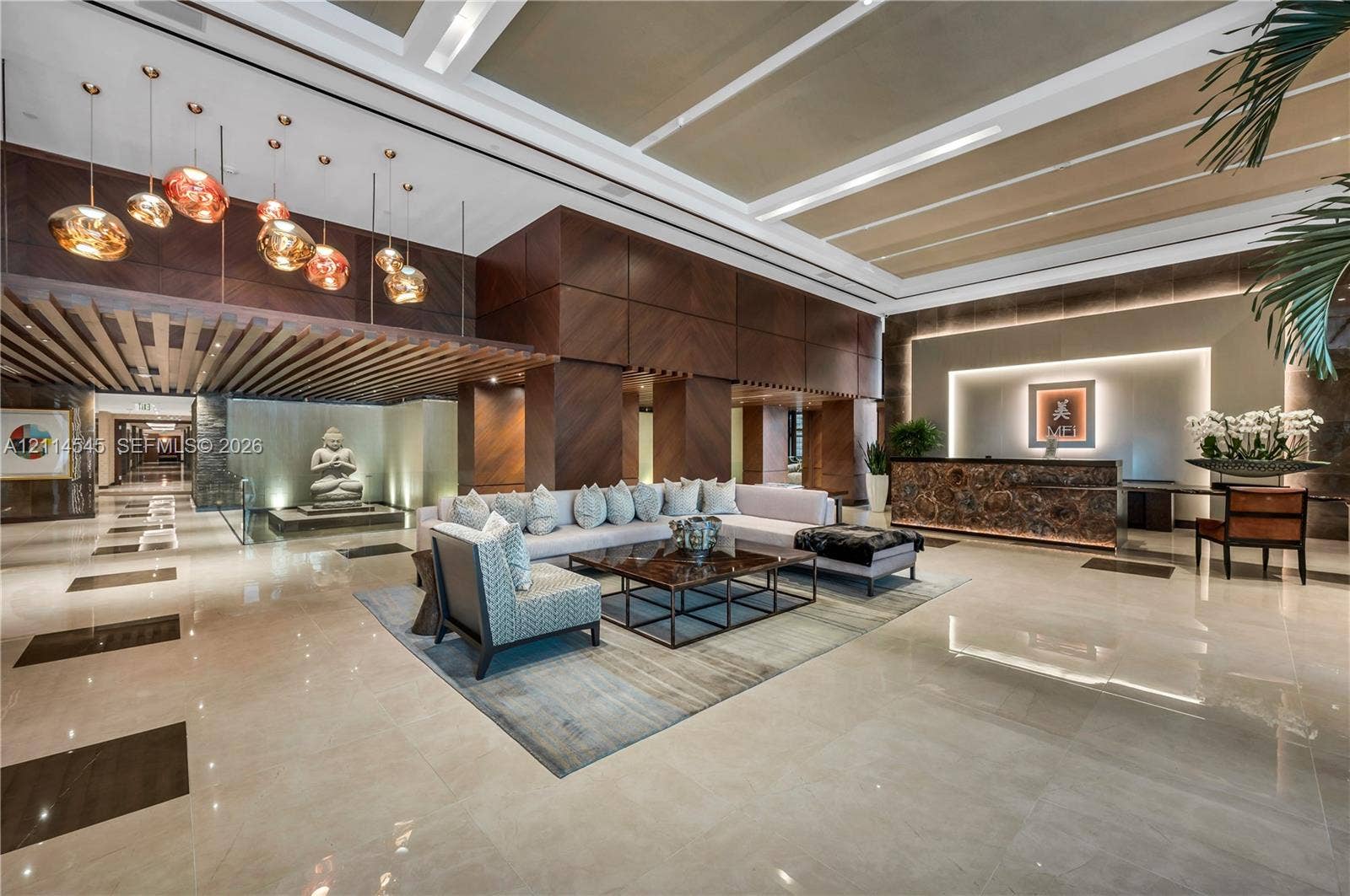 5875 Collins Avenue, #1503, Miami Beach, FL 33140 Grand lobby featuring high coffered ceilings, large-format tile flooring, wood-paneled walls, an integrated reception desk with stone detailing, and multi-pendant lighting fixtures
