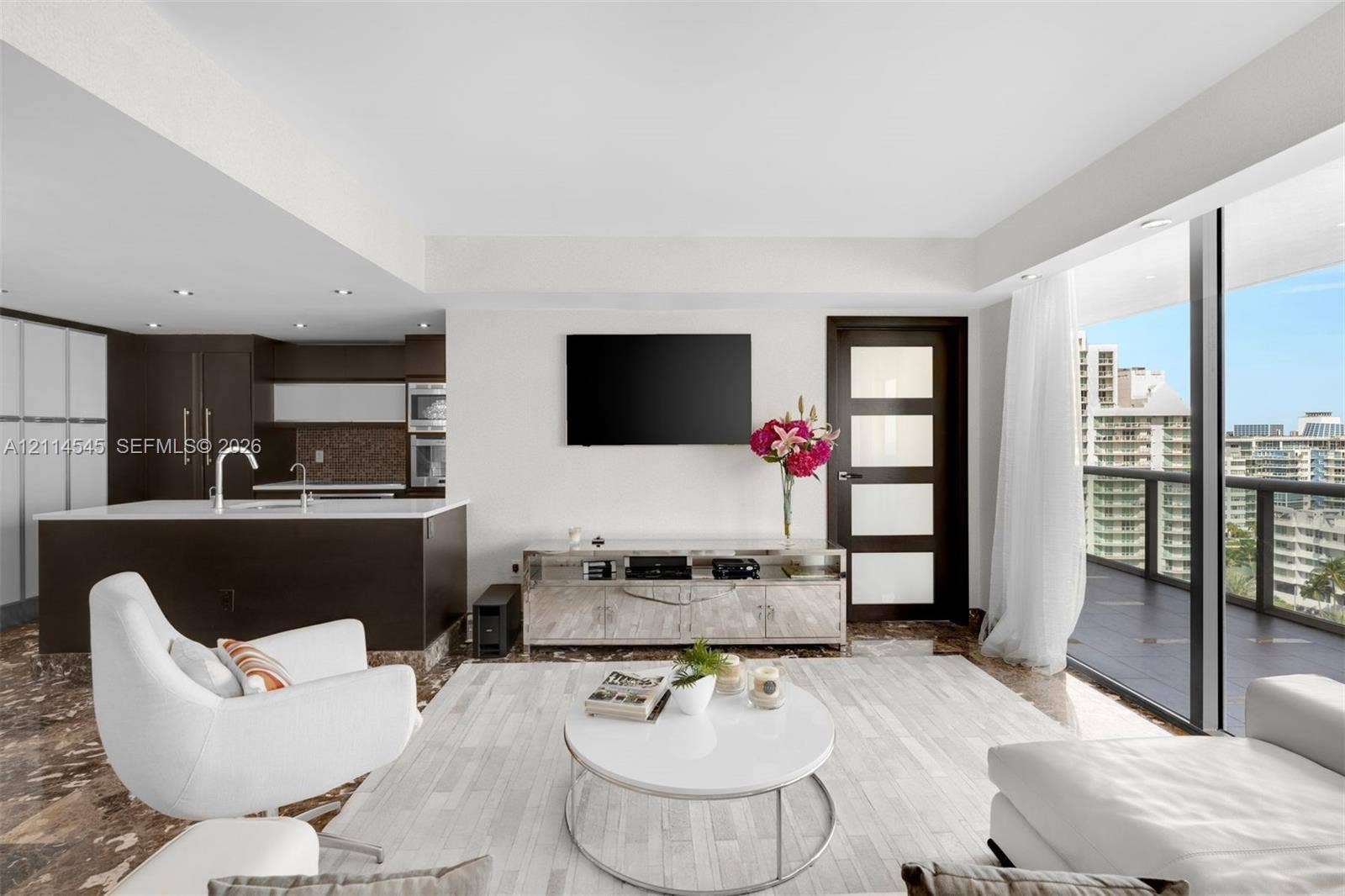 5875 Collins Avenue, #1503, Miami Beach, FL 33140 Open-concept living space featuring stone flooring, a kitchen island with integrated sink, recessed ceiling lighting, a five-panel frosted glass door, and expansive floor-to-ceiling windows leading to a covered balcony