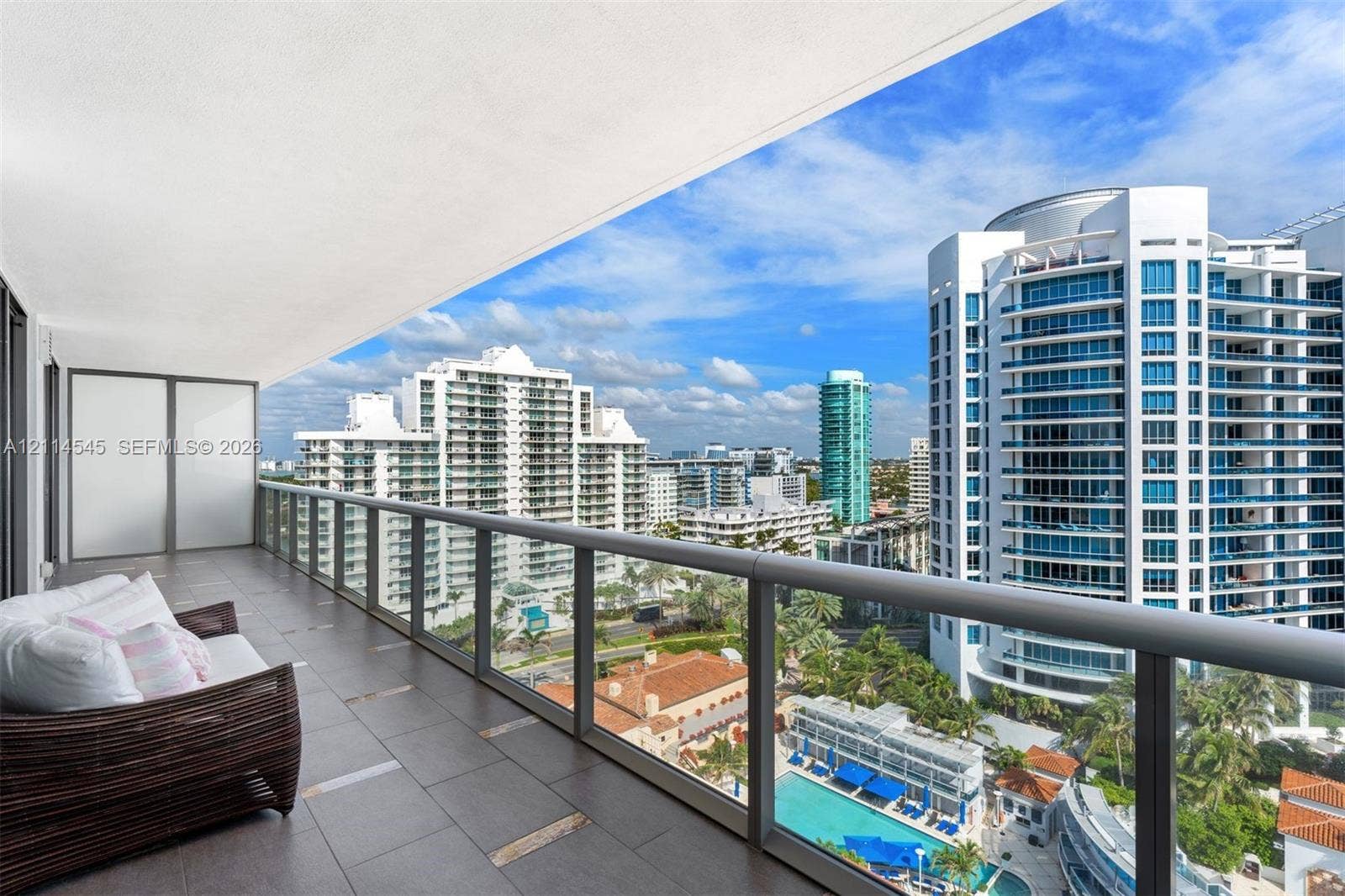 5875 Collins Avenue, #1503, Miami Beach, FL 33140 Covered terrace featuring dark tile flooring and a glass railing system, overlooking urban architecture and a swimming pool