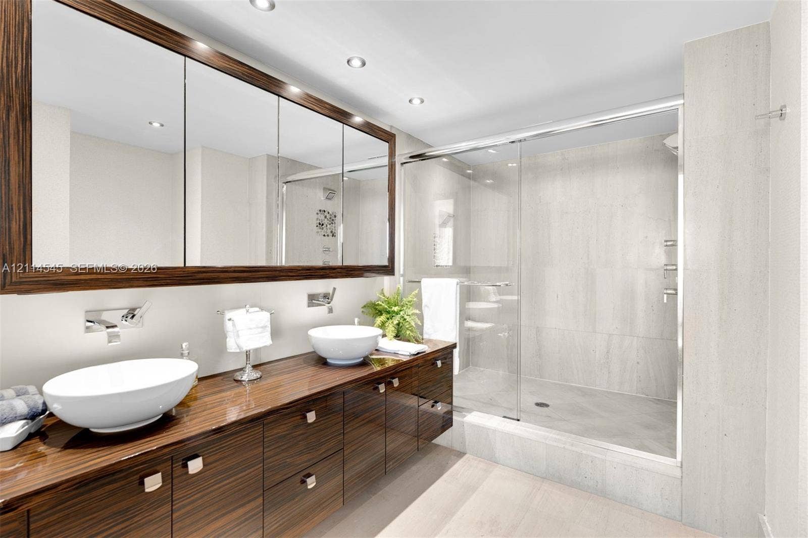 5875 Collins Avenue, #1503, Miami Beach, FL 33140 Dual-sink vanity featuring a dark wood finish, two white vessel sinks, wall-mounted chrome faucets, and an expansive tri-panel medicine cabinet